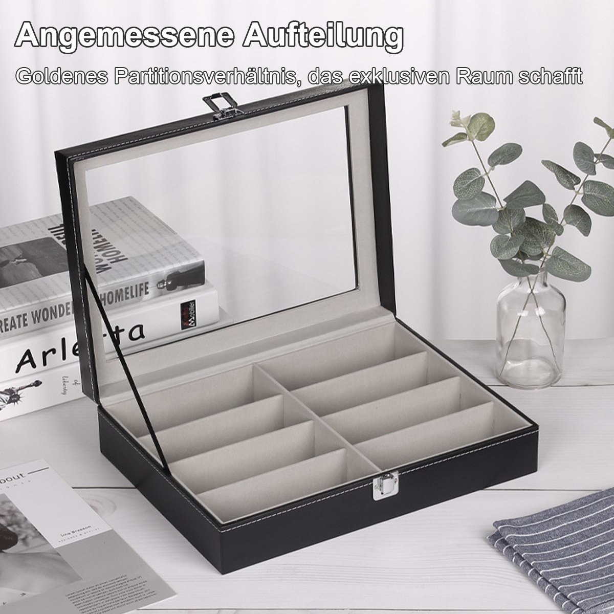 Offene, schwarze Brillenetui mit Fächern. Bücher und eine Vase mit grünen Blättern im Hintergrund auf weißer Holzoberfläche.