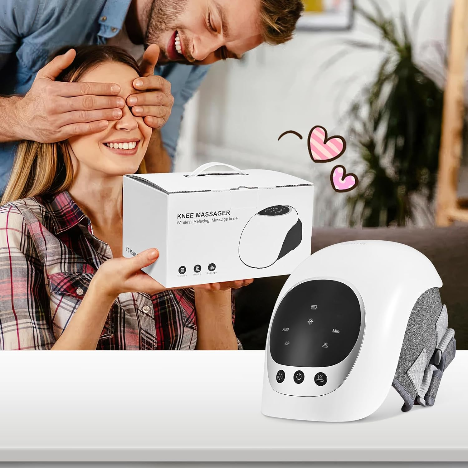 Ein Mann bedeckt die Augen einer Frau. Sie lächelt und hält eine Knie-Massagegerät-Box, während ein weiteres Massagegerät auf einem Tisch steht. Rosa Herzen schweben darüber.