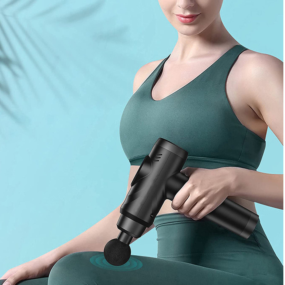 Eine Frau in tealfarbener Sportkleidung hält eine schwarze Massagepistole und verwendet sie an ihrem Oberschenkel. Der Hintergrund ist hellblau.