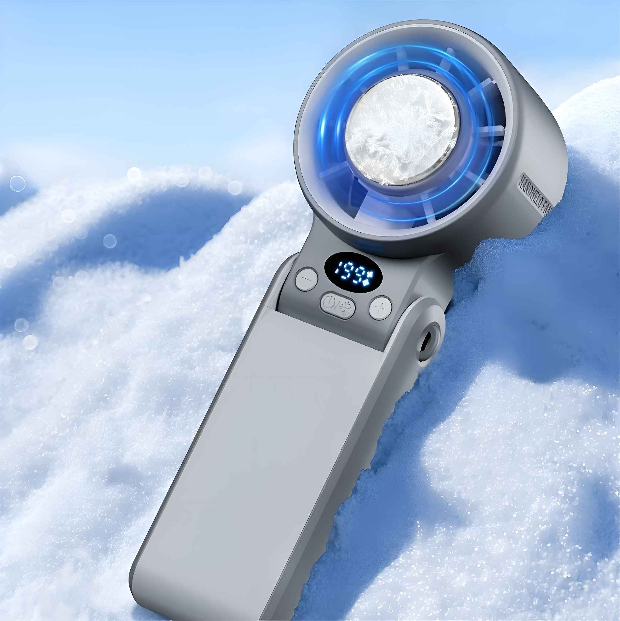 Ein grauer Handventilator mit blauem Licht liegt auf schneebedecktem Boden. Das Display zeigt '199'.