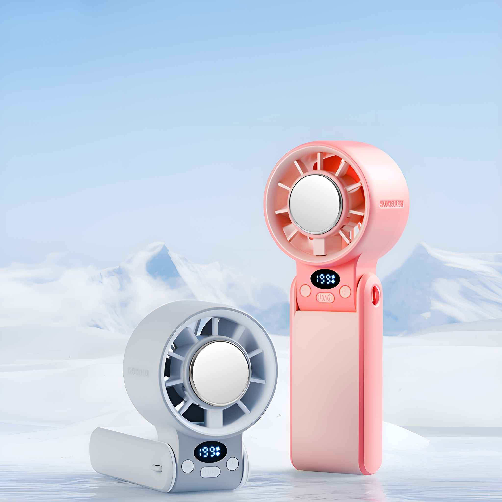 Zwei tragbare Ventilatoren, einer rosa und einer grau, vor dem Hintergrund eines schneebedeckten Berges und eines blauen Himmels.