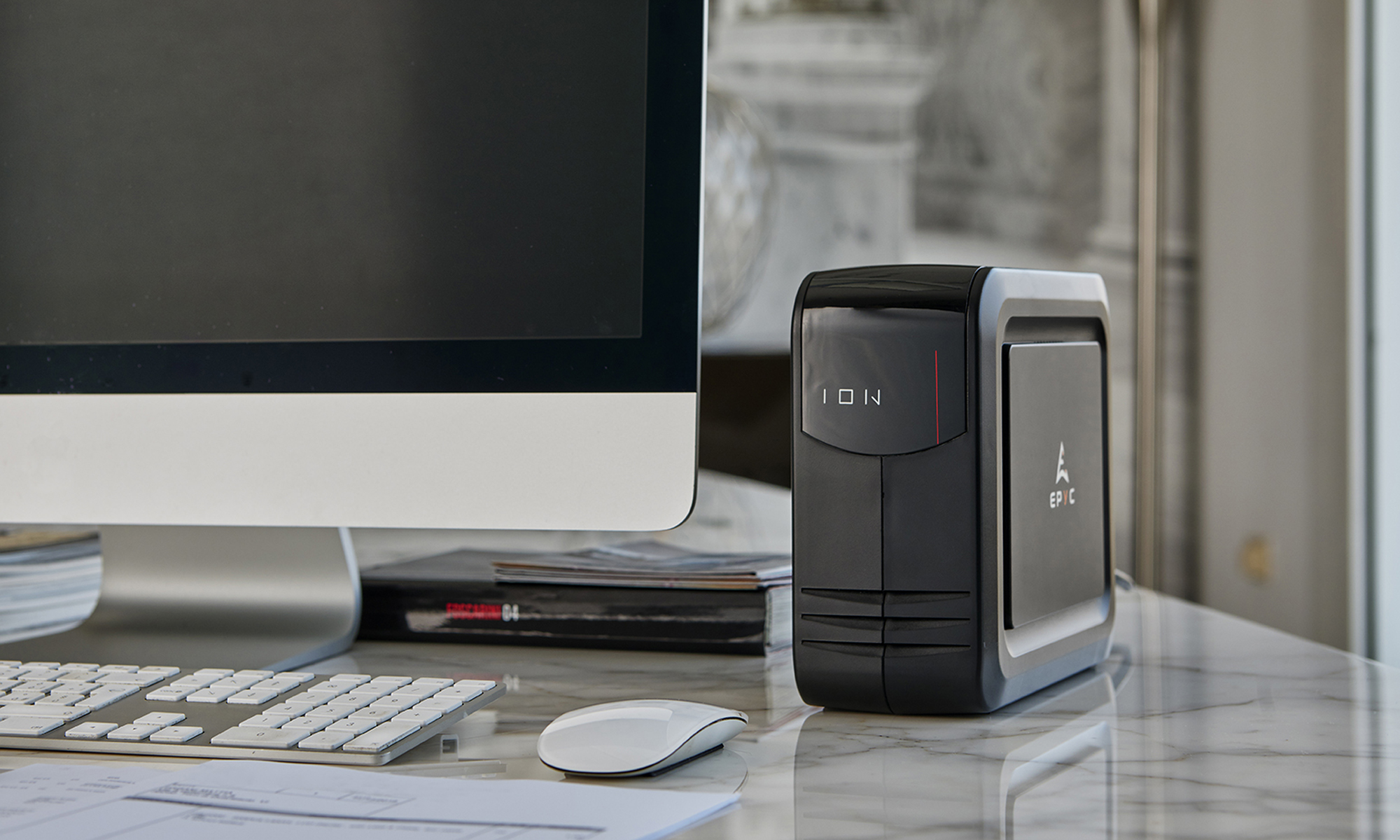 Un'installazione computer con monitor, tastiera, mouse e un server nero. La scrivania ha un motivo marmorizzato.