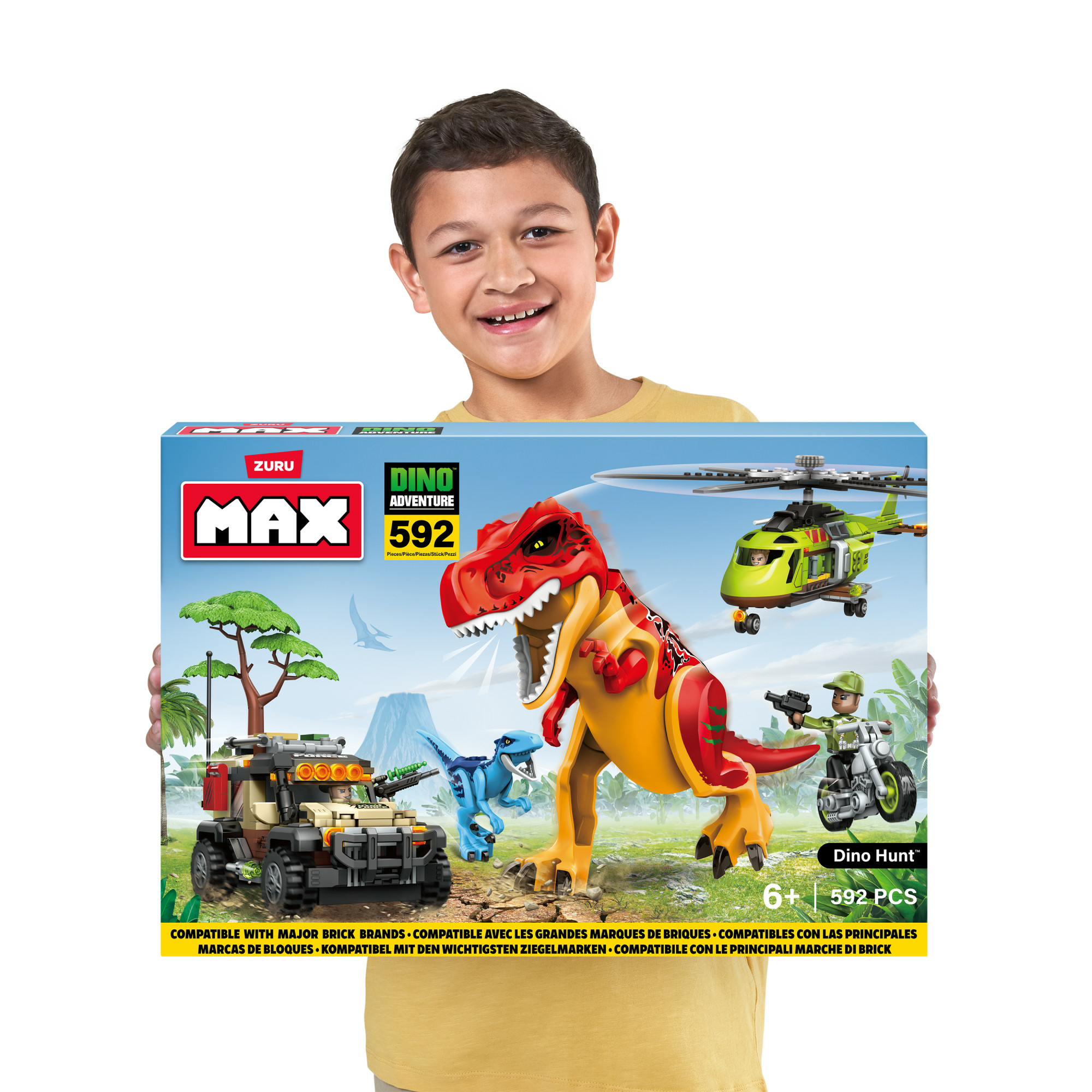 Dziecko trzyma pudełko z zabawkami z motywem dinozaurów. Na pudełku widnieje czerwony T-Rex, helikopter i zabawkowy jeep. Dziecko się uśmiecha.