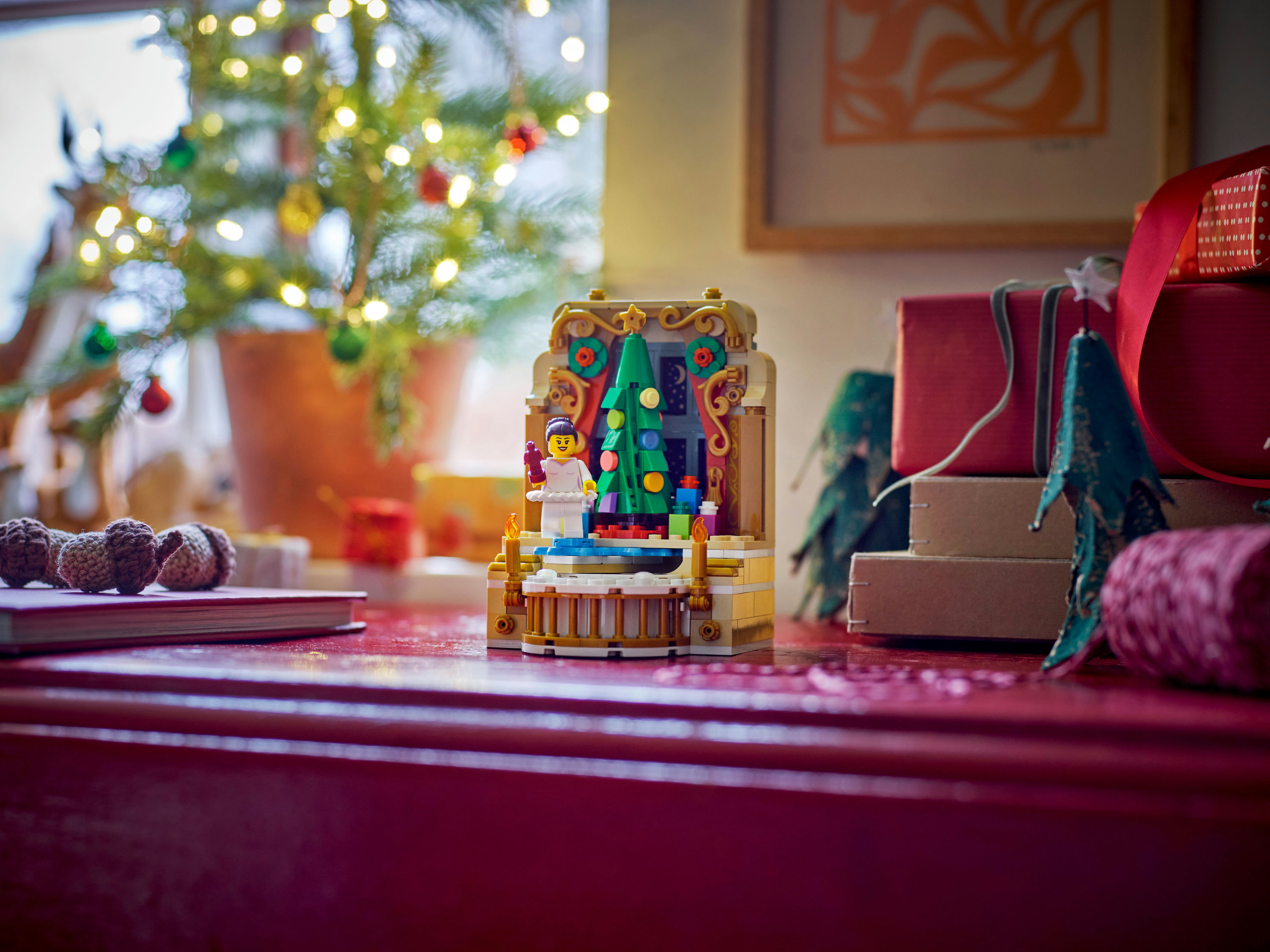 Eine Weihnachtsszene mit einem Lego-Set, Baum, Geschenken und Ornamenten auf roter Oberfläche.