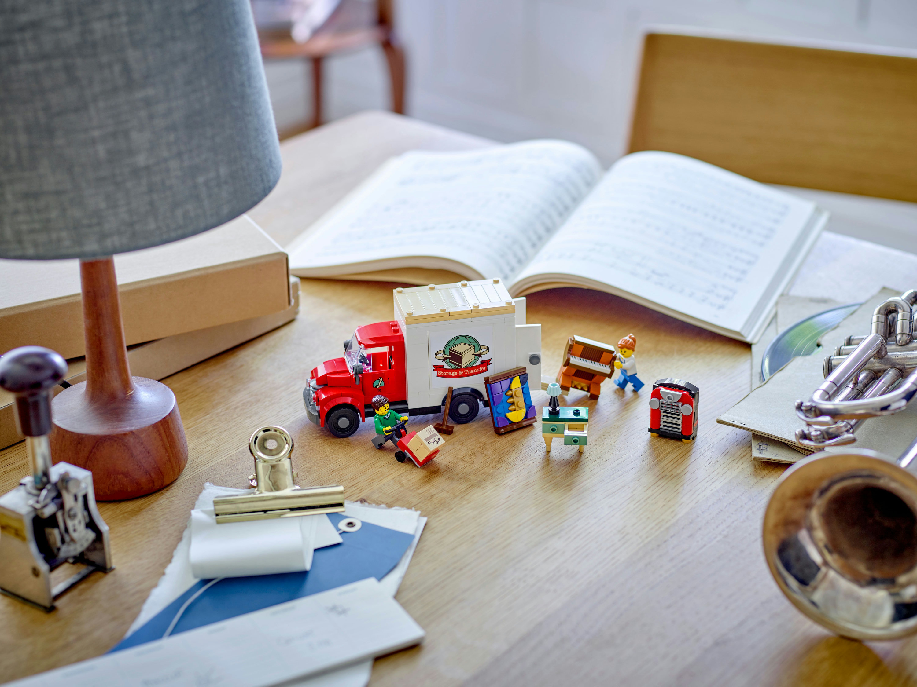 Lego-Szene auf einem Holztisch. Enthält einen Umzugswagen, Musikinstrumente, Noten und Miniaturmöbel.
