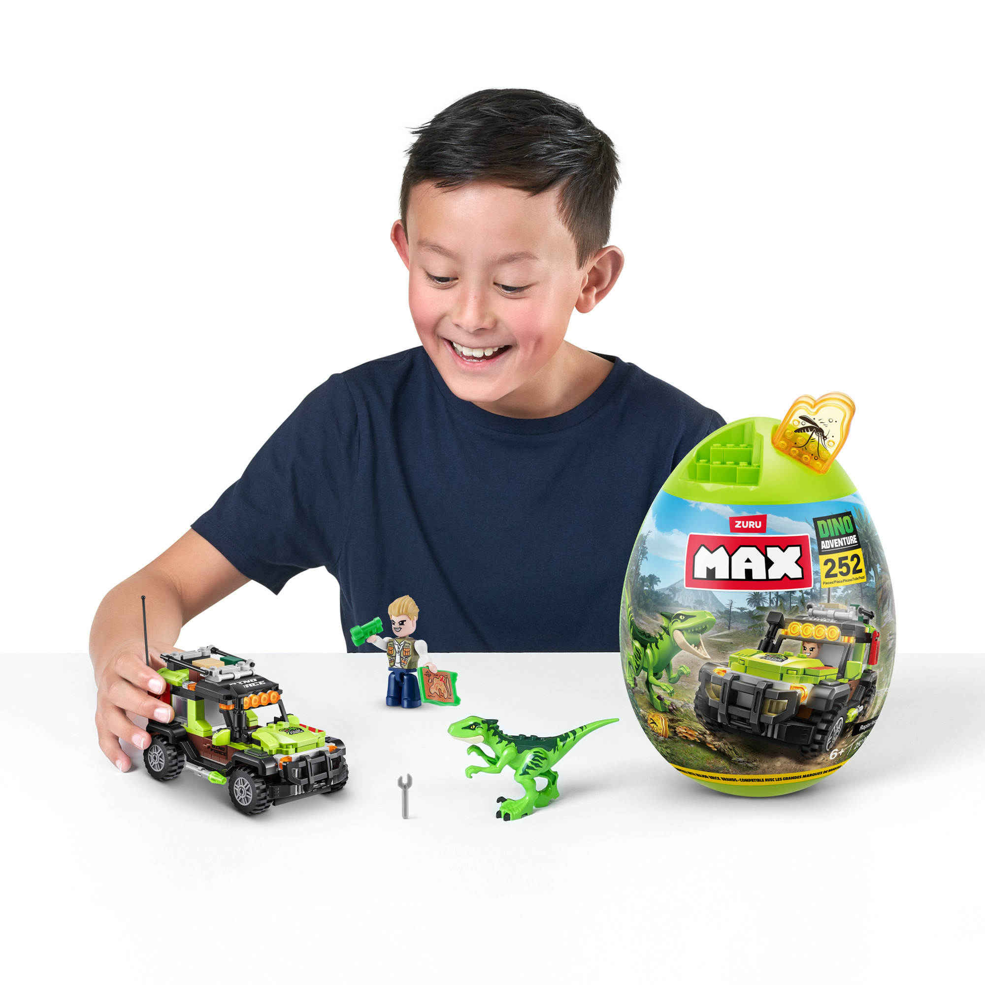 Un bambino sorride a un set di giocattoli Dino Adventure. Include un'auto giocattolo, un dinosauro, un uovo e una piccola figura.