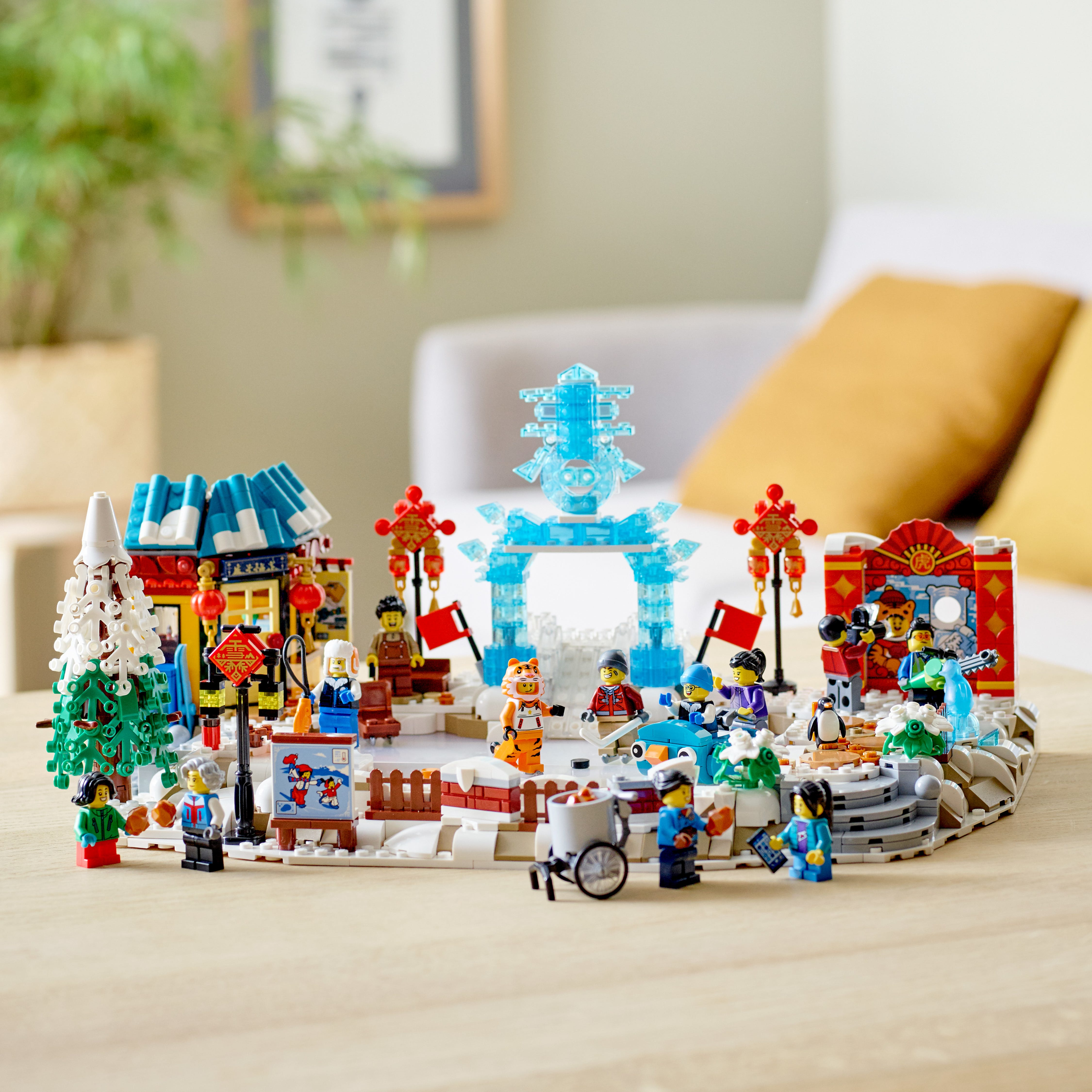 Un set Lego raffigura un festival invernale con edifici, persone e una figura di tigre. La scena è ambientata su un tavolo di legno.