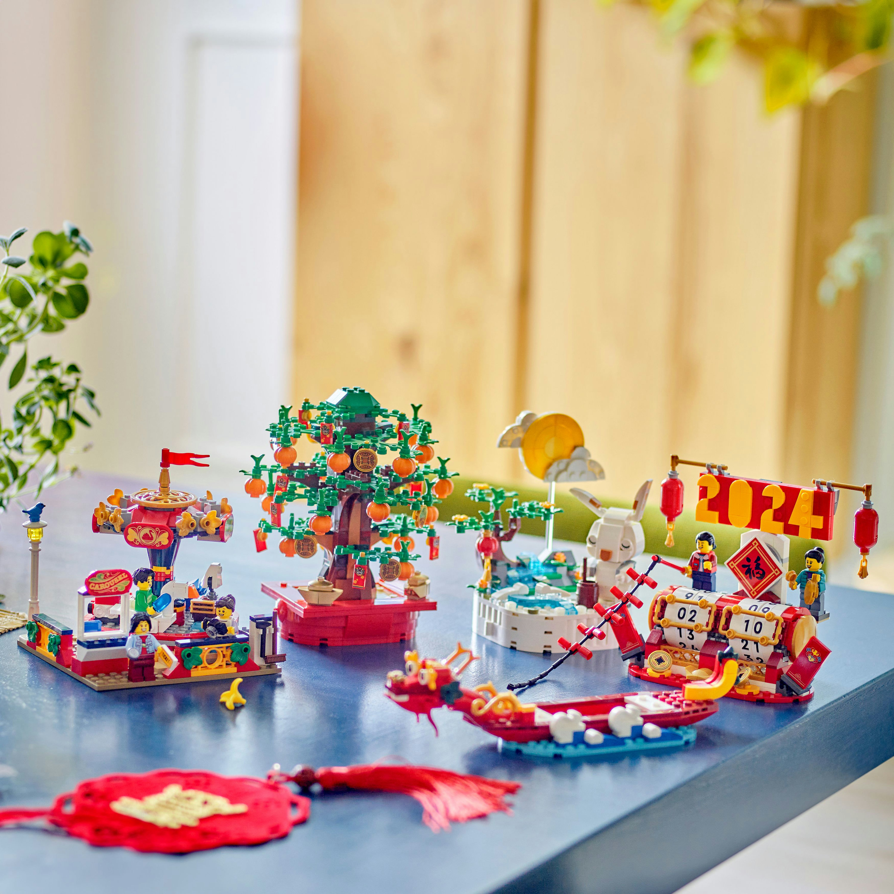 Un set Lego che raffigura scene del capodanno lunare, tra cui un albero con arance, una giostra e una barca drago, il tutto su un tavolo blu.