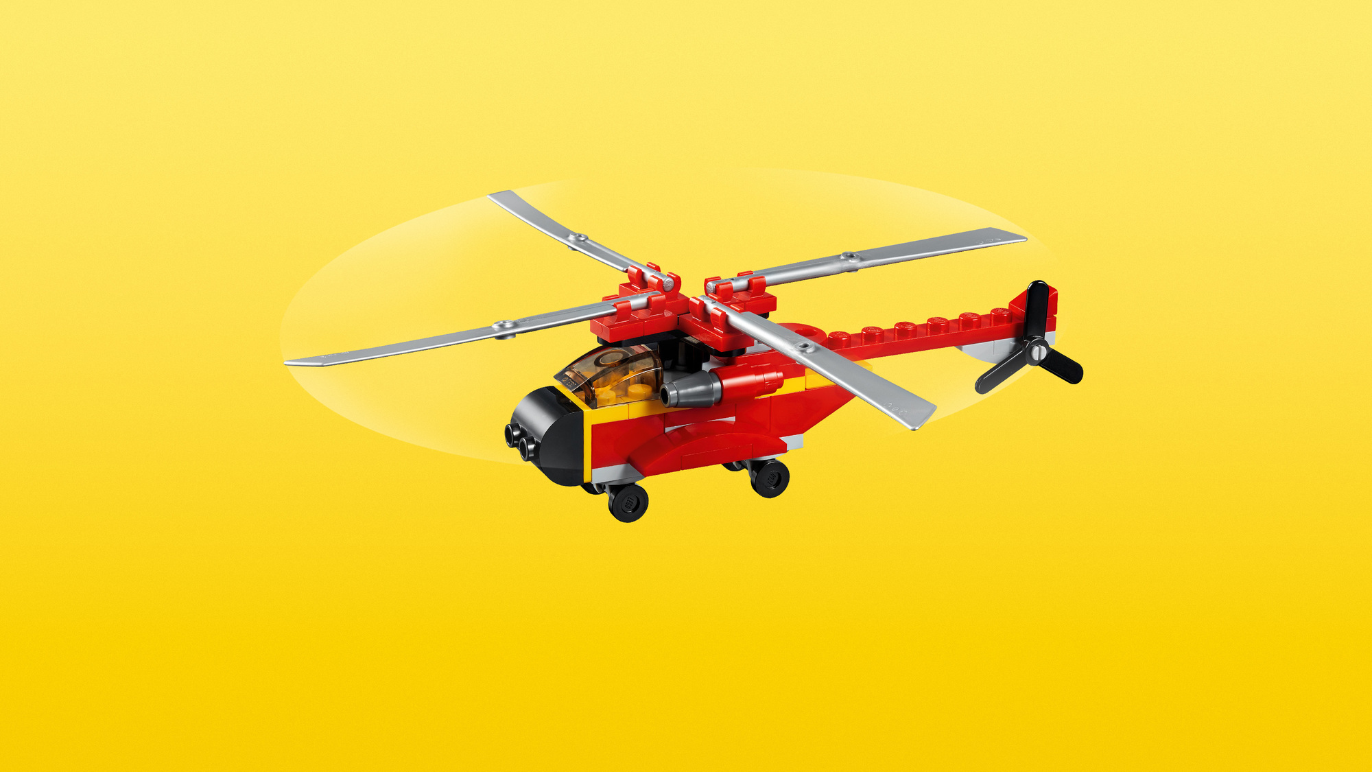 Czerwono-żółty helikopter zabawka z obracającymi się łopatami i czarnym wirnikiem ogonowym na żółtym tle.
