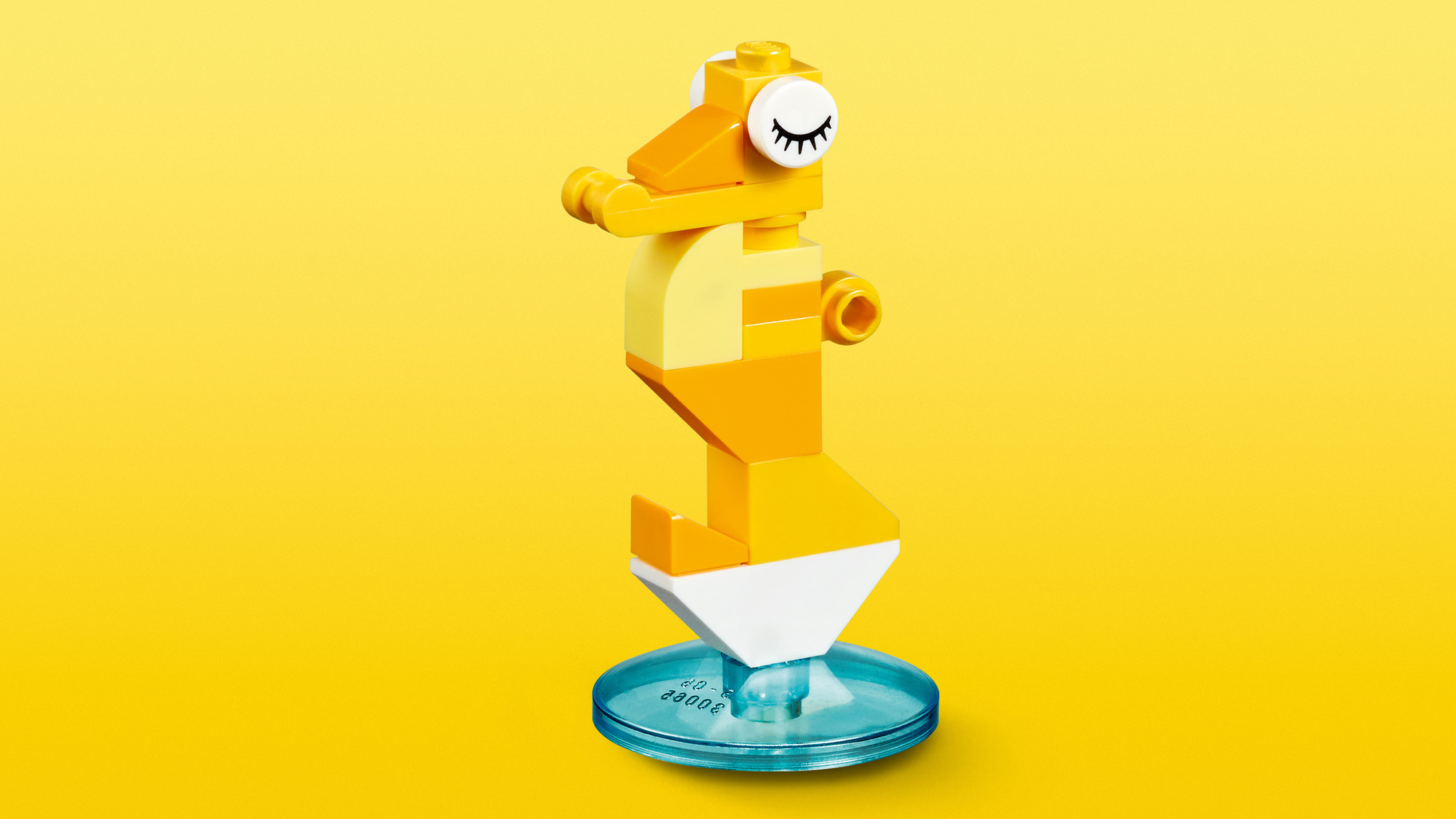 Koniu morski Lego z żółtymi i pomarańczowymi klockami, białym brzuchem i niebieską, przezroczystą podstawą na żółtym tle.