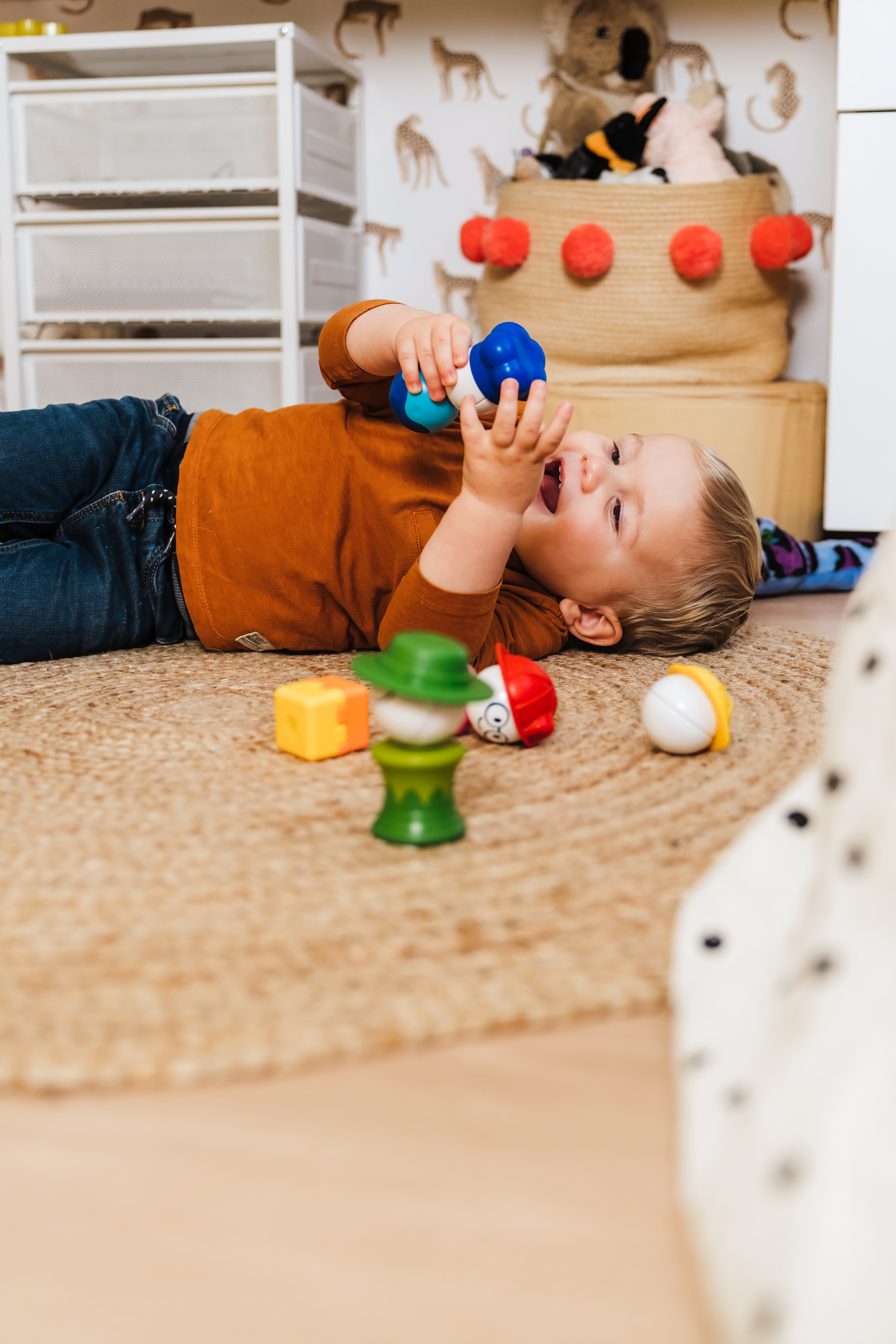 Un bambino gioca con un giocattolo blu e bianco su un tappeto. I giocattoli sono sparsi.