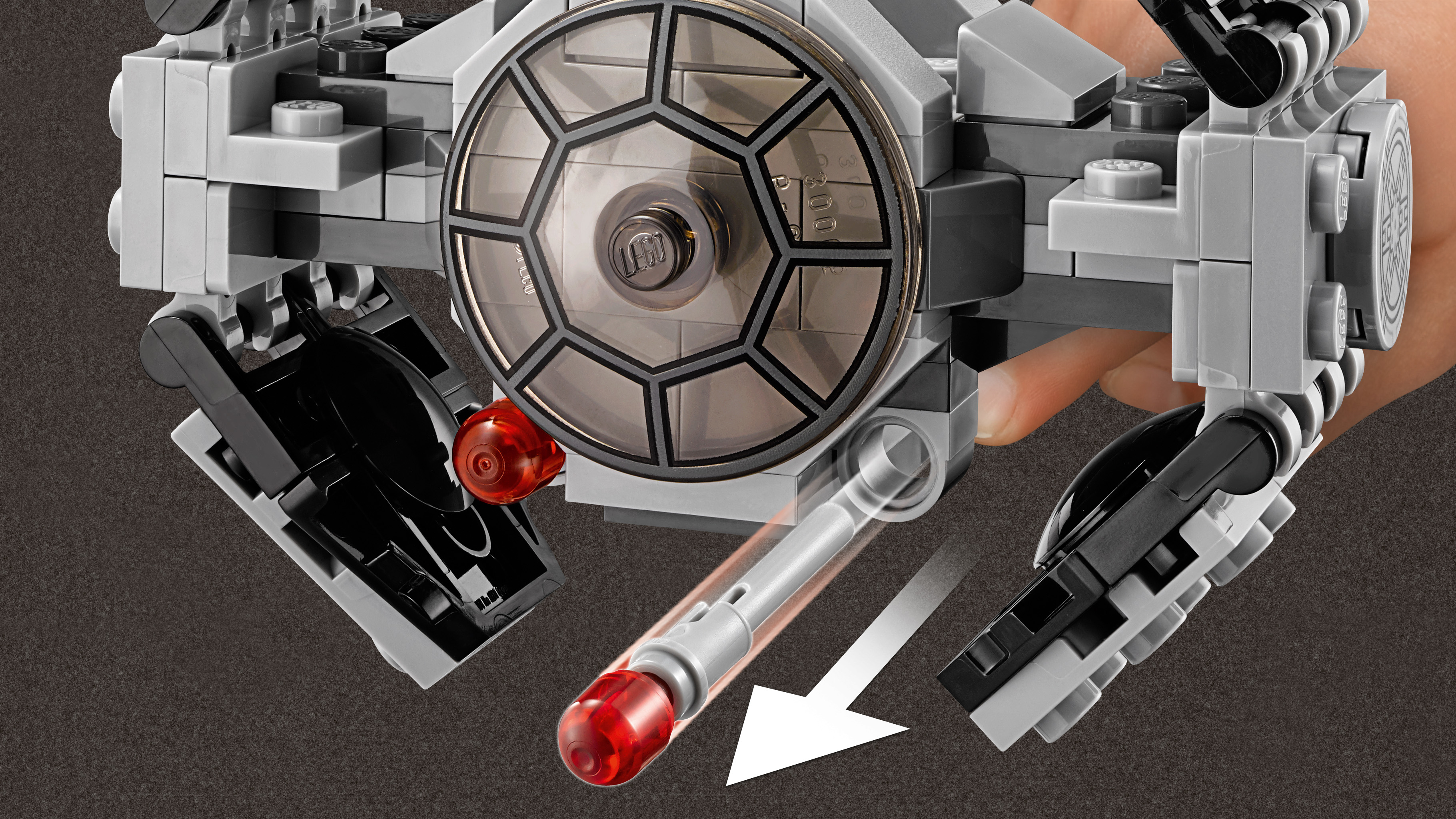 Un modello LEGO TIE fighter con cabina di pilotaggio trasparente. Una mano tiene un missile grigio con la punta rossa, con una freccia che indica il movimento.