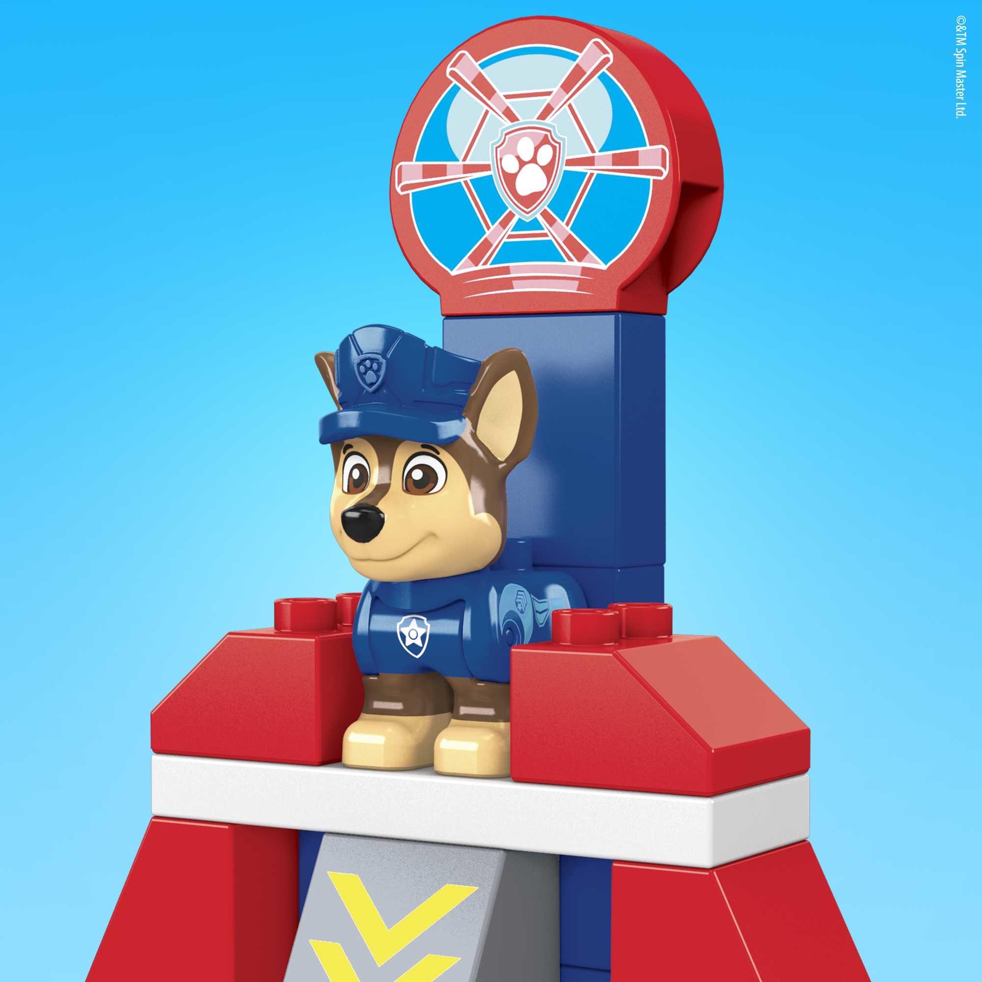 Una figura giocattolo di Chase di Paw Patrol su una struttura rossa, blu e bianca contro uno sfondo blu.