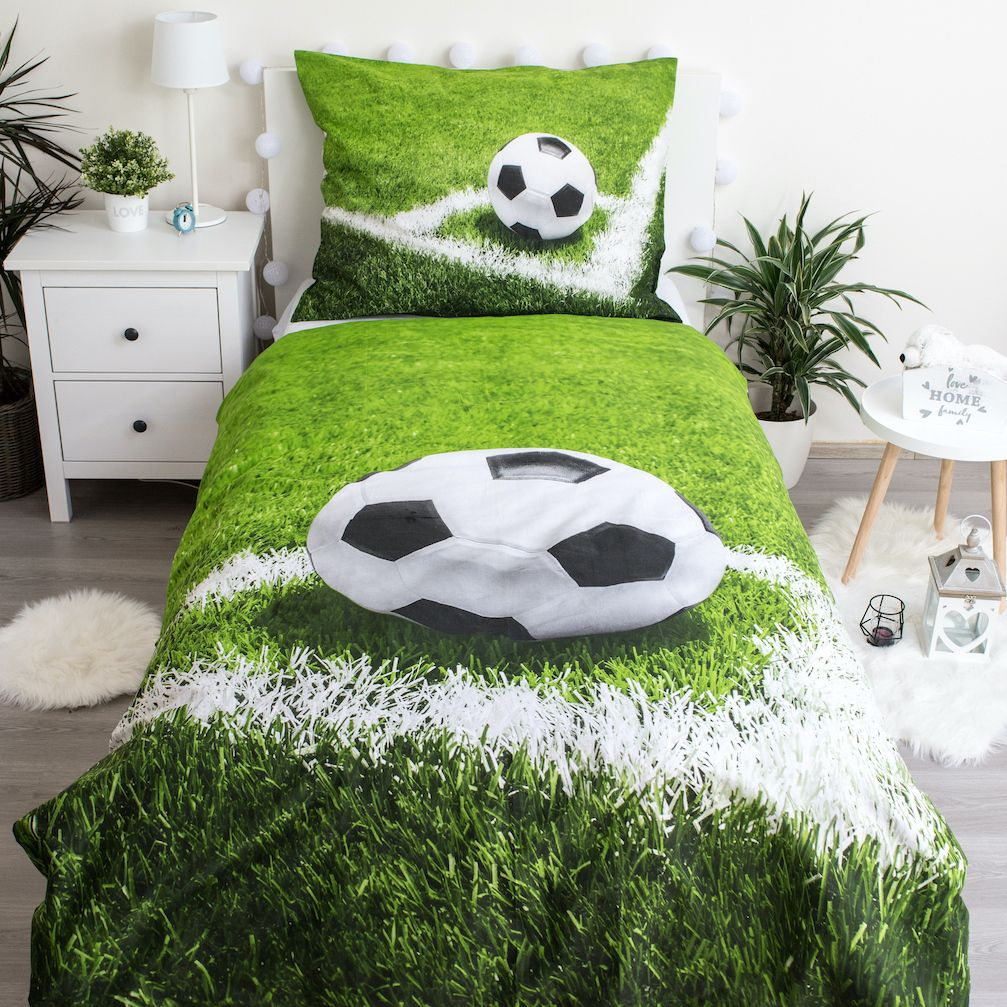 Ein Bett mit Fußball-Motiv, grünes Gras-Design. Ein Fußballkissen und ein Fußball auf dem Kissen. Weißer Nachttisch mit Lampe.