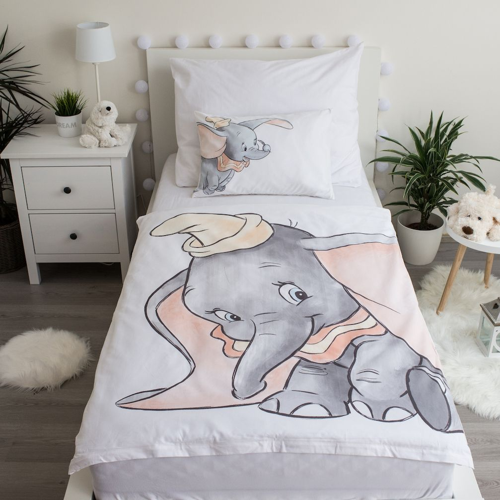 Bett mit Dumbo-Bettwäsche und Kissen. Eine kleine Lampe und ein Beistelltisch mit einem Stofftier stehen daneben.