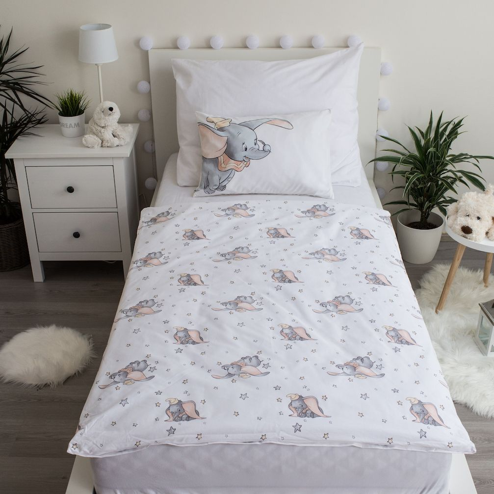 Ein Bett mit Dumbo-Bettwäsche. Ein weißer Nachttisch, Pflanzen und ein kleiner weißer Teppich vervollständigen die Szene.