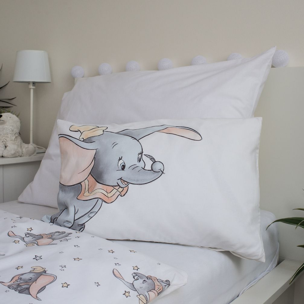 Ein Bett mit einem Kissen mit Dumbo. Es gibt andere Elemente wie eine Lampe, einen Teddybären und eine Decke mit Dumbo-Mustern.
