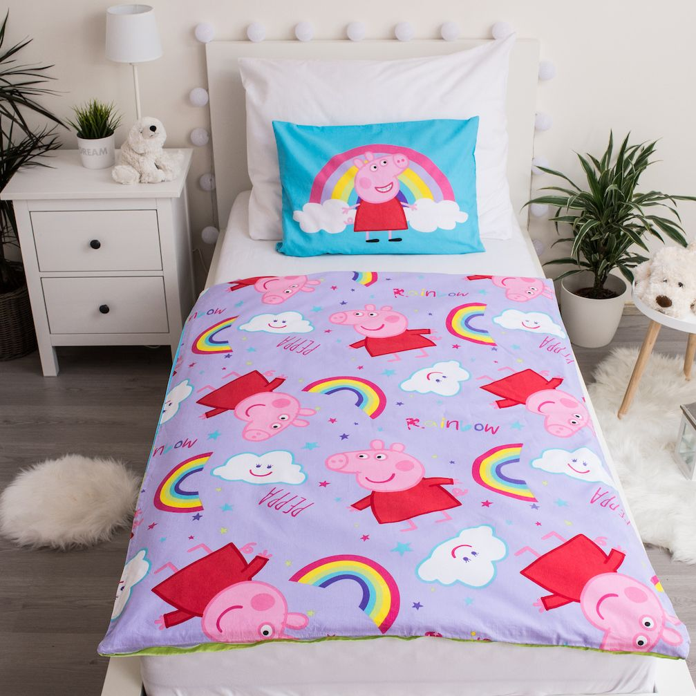 Ein Kinderbett mit Peppa Wutz-Motiv. Die Bettwäsche umfasst ein Kissen und einen Bettbezug mit Peppa Wutz- und Regenbogenmustern. Weiße Möbel umgeben es.