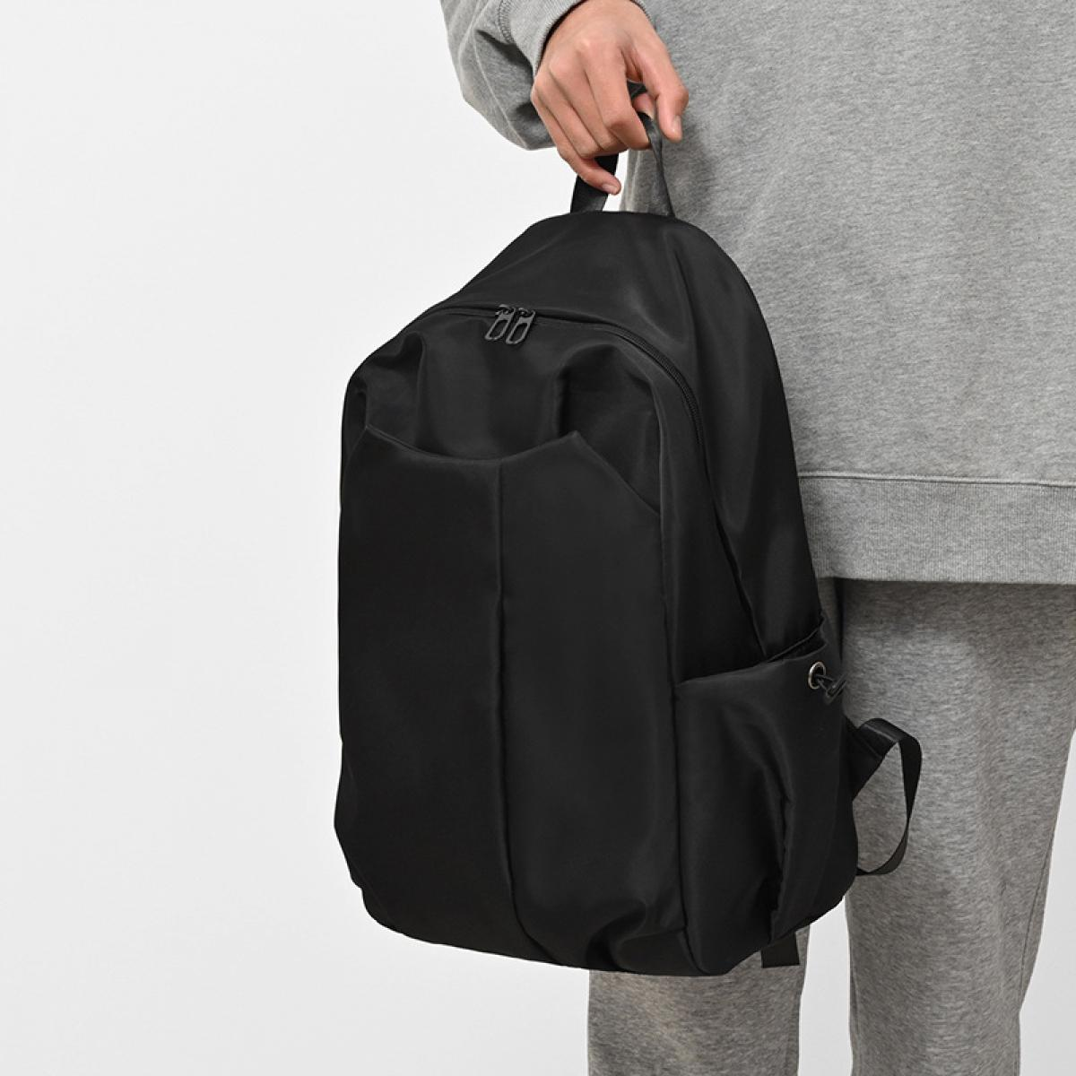Eine Person hält einen schwarzen Rucksack. Die Person trägt eine graue Jogginghose und einen Sweatshirt. Der Hintergrund ist weiß.