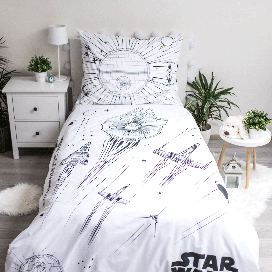 Ein Bett mit einer Star Wars-Bettwäsche. Die Bettwäsche zeigt Illustrationen von Raumschiffen und dem Todesstern auf weißem Grund.