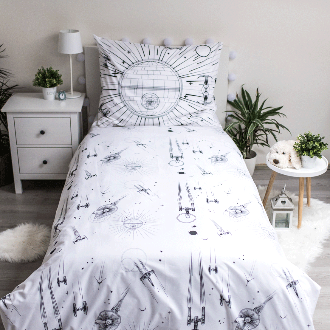 Ein Bett mit einem Star Wars-Bettbezug und -Kissen. Der Bezug zeigt Illustrationen von Raumschiffen und dem Todesstern.