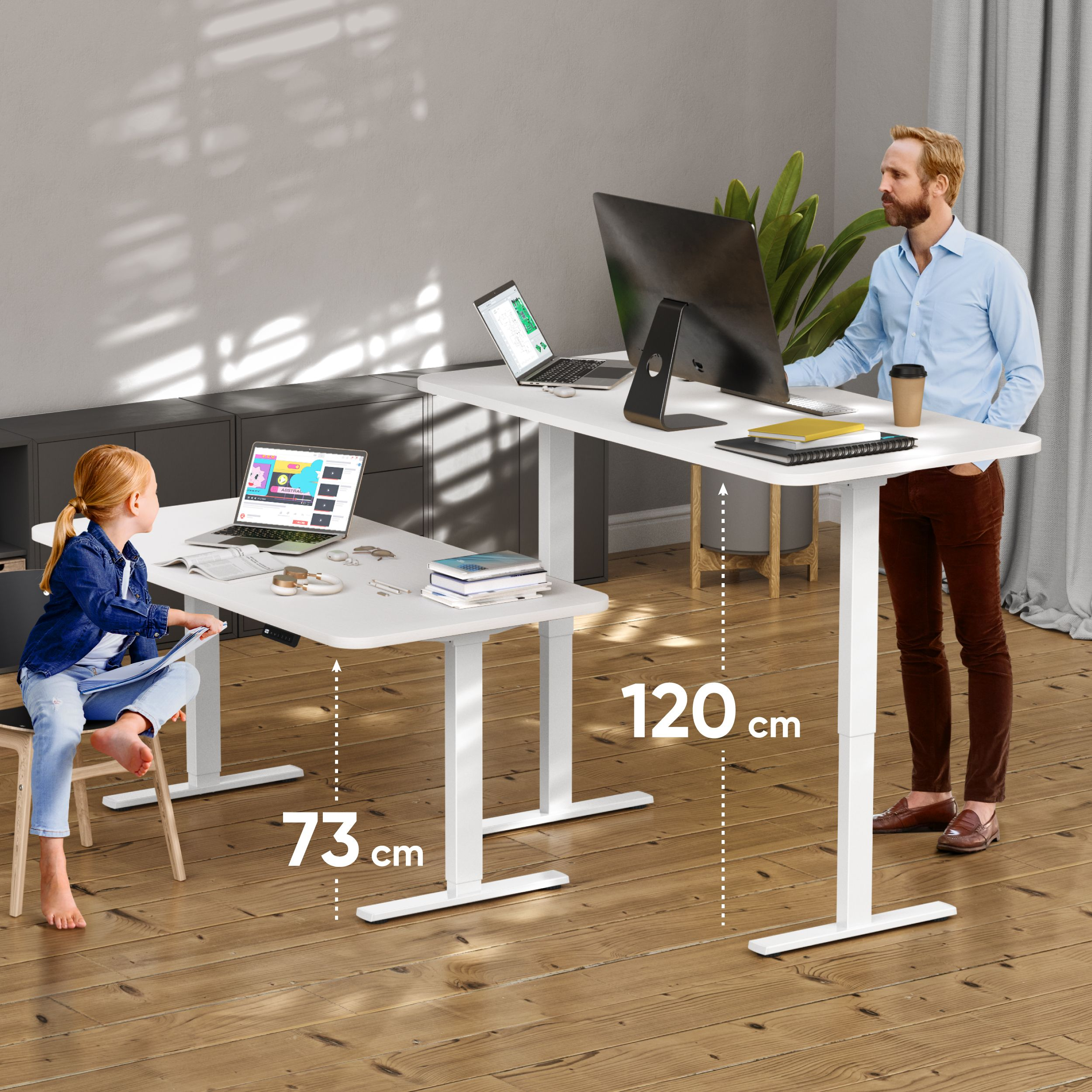 Ein Mann und ein Mädchen sitzen an höhenverstellbaren Schreibtischen mit Laptops. Der Mann steht, das Mädchen sitzt. Eine Pflanze, Kaffee und Monitor sind vorhanden.