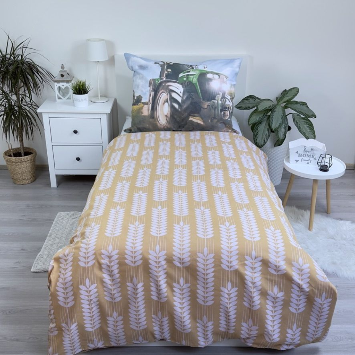 Ein Bett mit Traktorkissen, Bettwäsche mit Weizenmuster, weißem Nachttisch und Pflanzen. Ein kleiner Tisch mit Kerzenhalter.