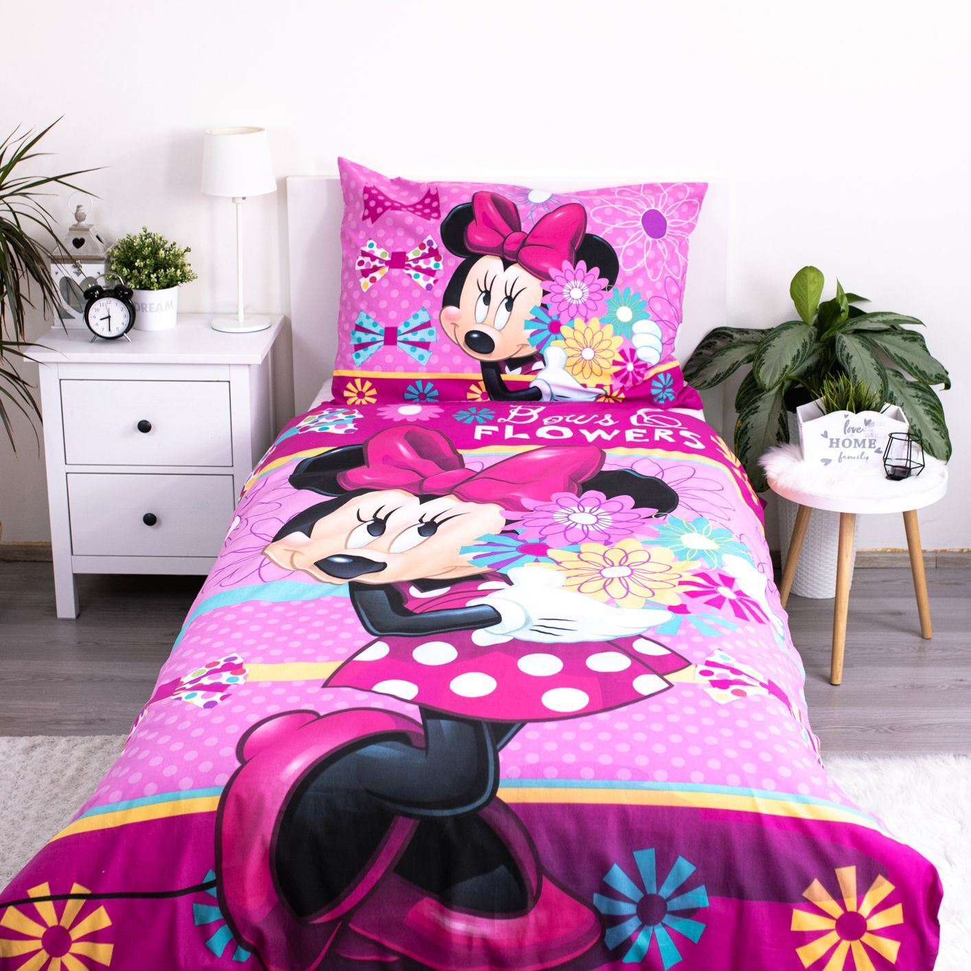 Minnie-Mouse-Bettwäsche in einem Zimmer. Rosa Bettwäsche mit Minnie Mouse darauf. Blumen und Schleifen sind ebenfalls auf der Bettwäsche zu sehen. Ein weißer Nachttisch ist sichtbar.