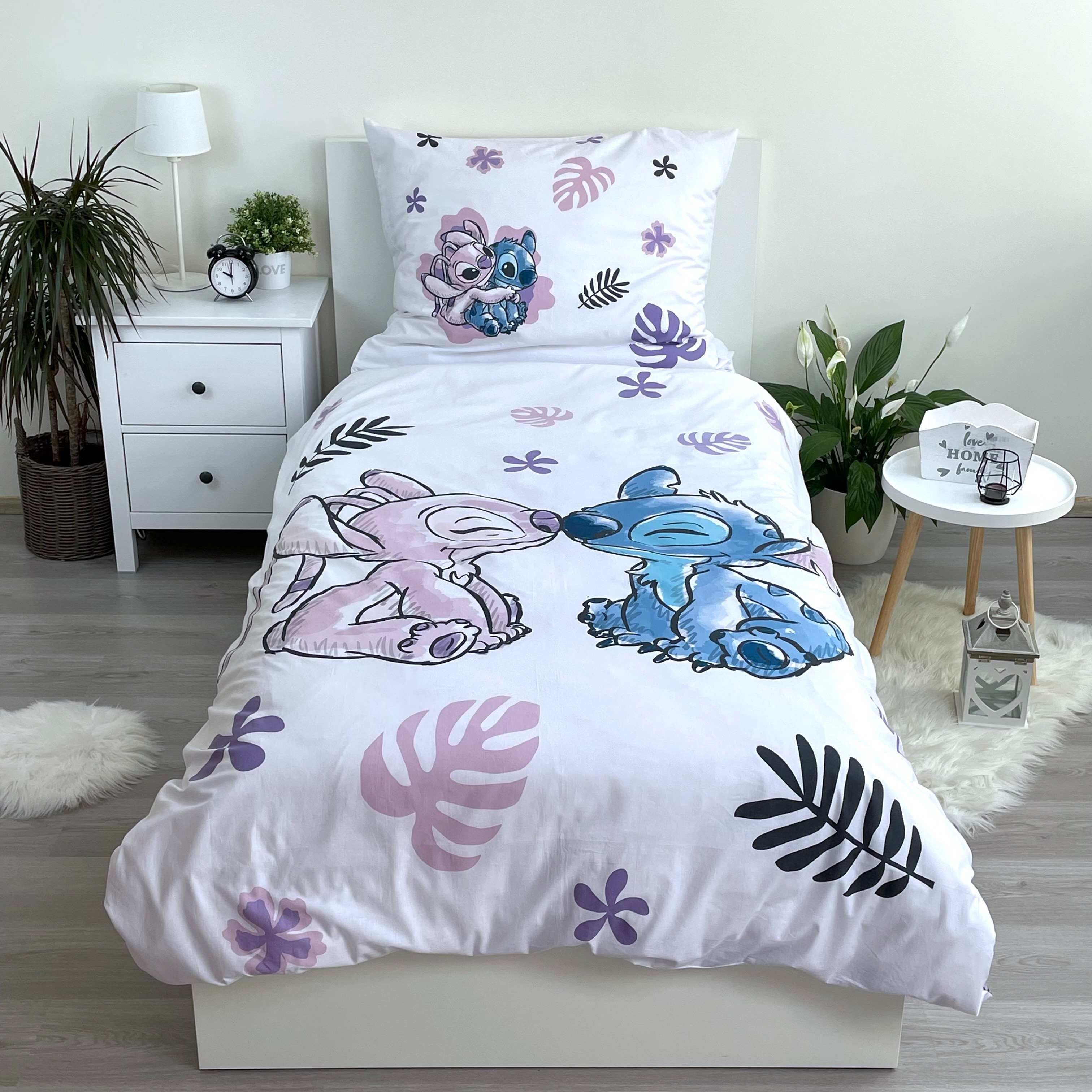 Weißes Bett mit Stitch-Bettwäsche. Nachttische mit Lampe, Pflanze und Wecker. Holzboden und ein weißer Teppich.
