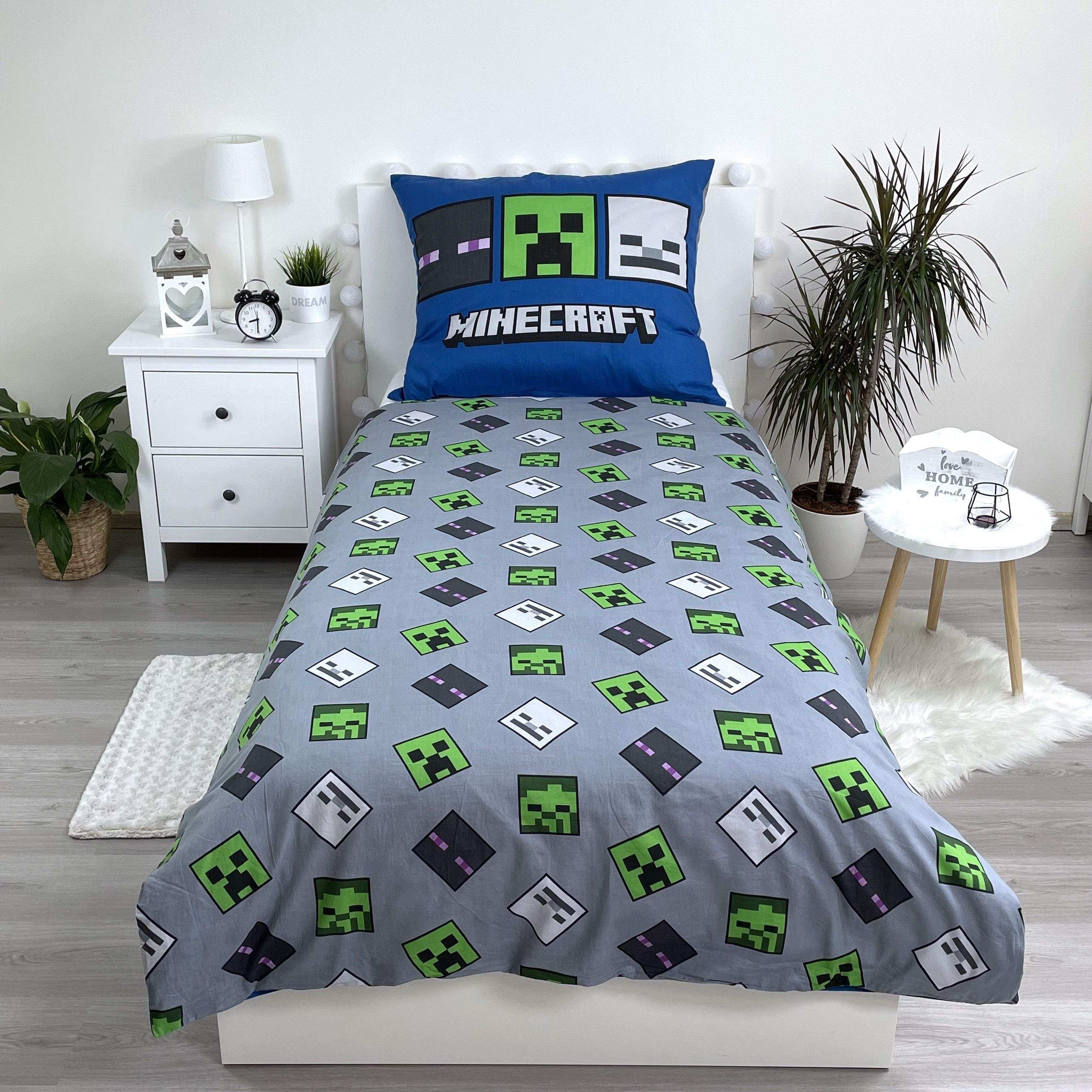 Ein Schlafzimmer mit Minecraft-Thema. Beinhaltet ein Bett mit Creeper-Kissen und Bettwäsche. Ein weißer Nachttisch, Pflanzen und ein kleiner Tisch sind ebenfalls sichtbar.
