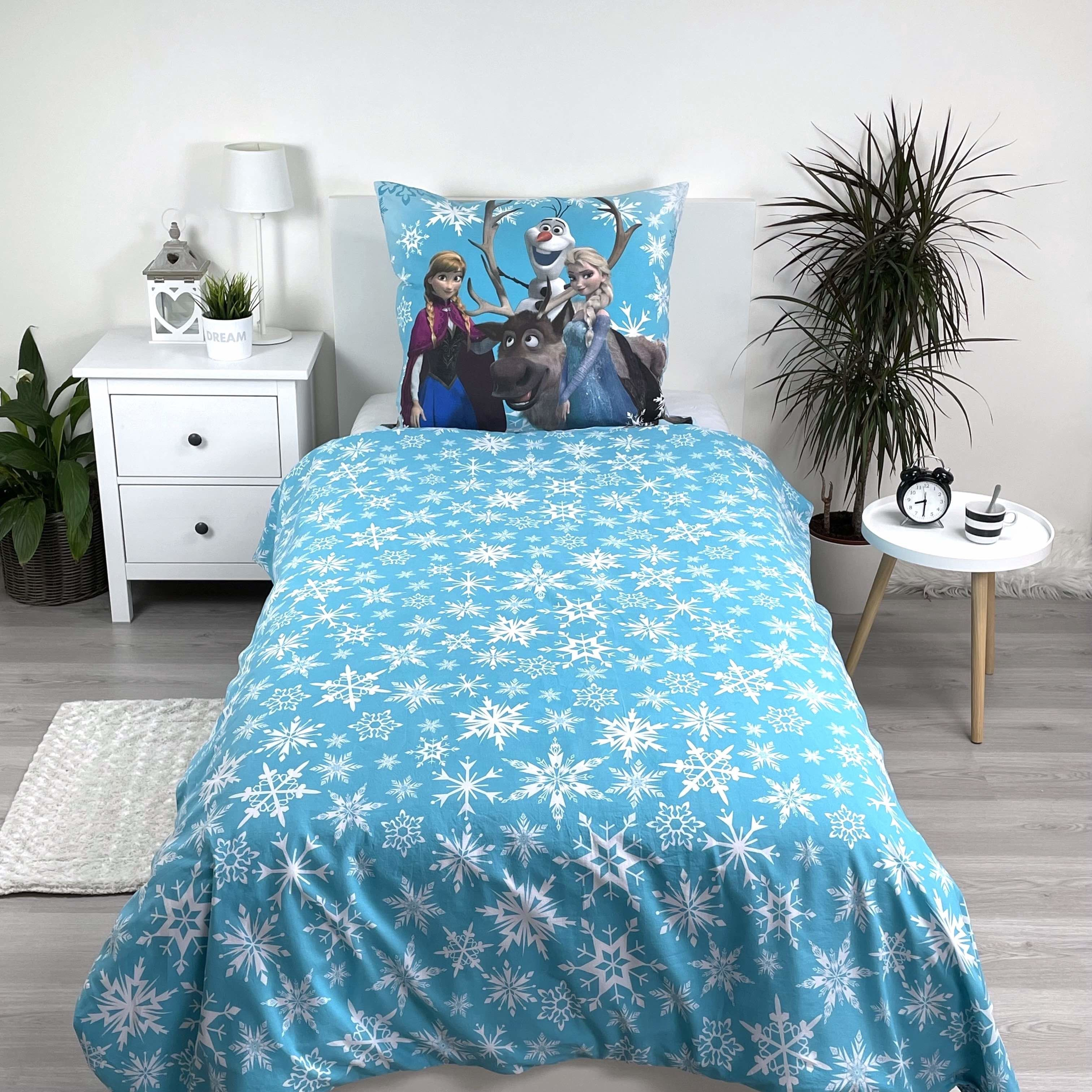 Ein Bett mit einer blauen Bettdecke mit weißen Schneeflocken. Ein Kissen mit Frozen-Figuren. Ein weißer Nachttisch.