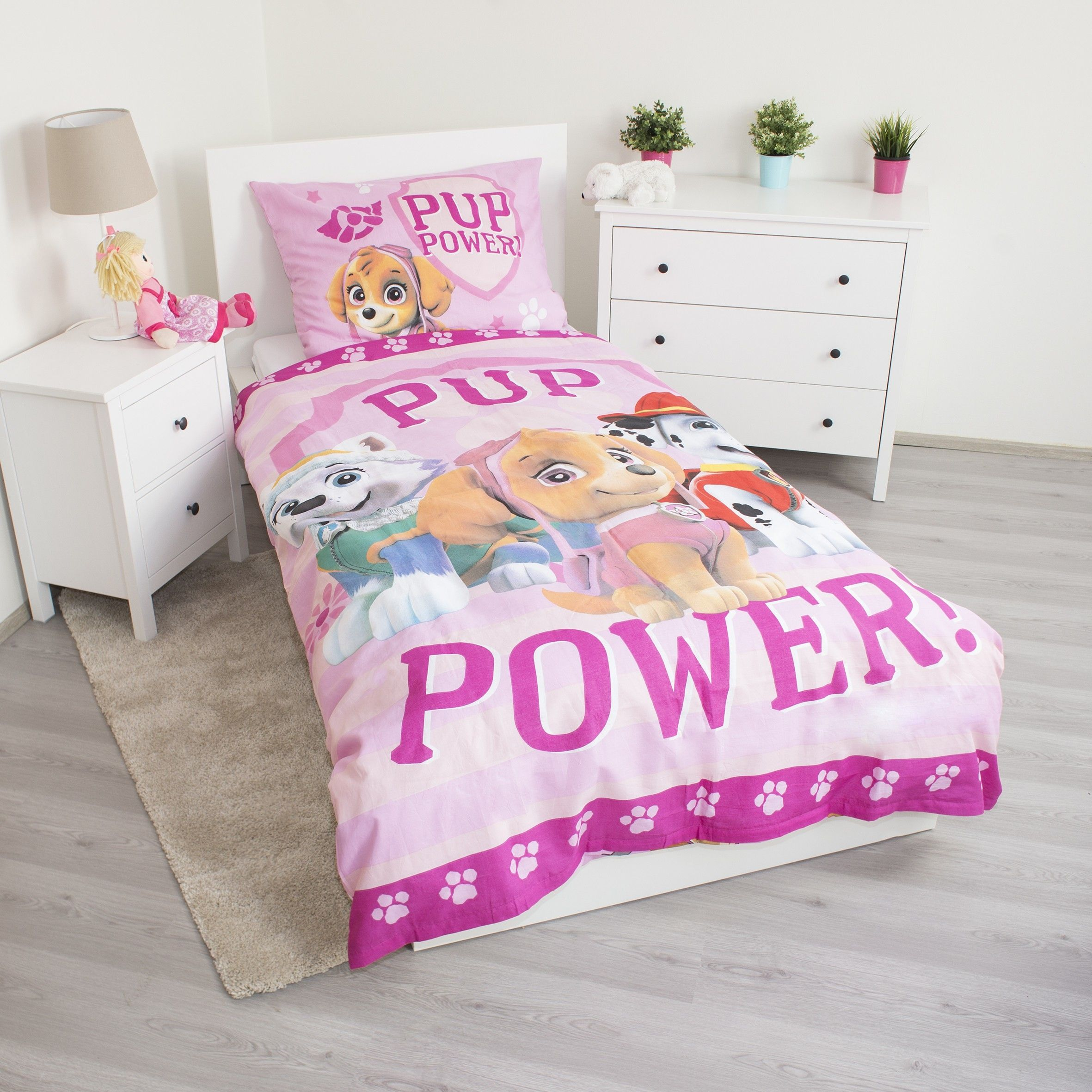 Ein Kinderzimmer mit einem Bett mit Paw Patrol-Bettwäsche. Ein Nachttisch mit Lampe und Puppe ist vorhanden.