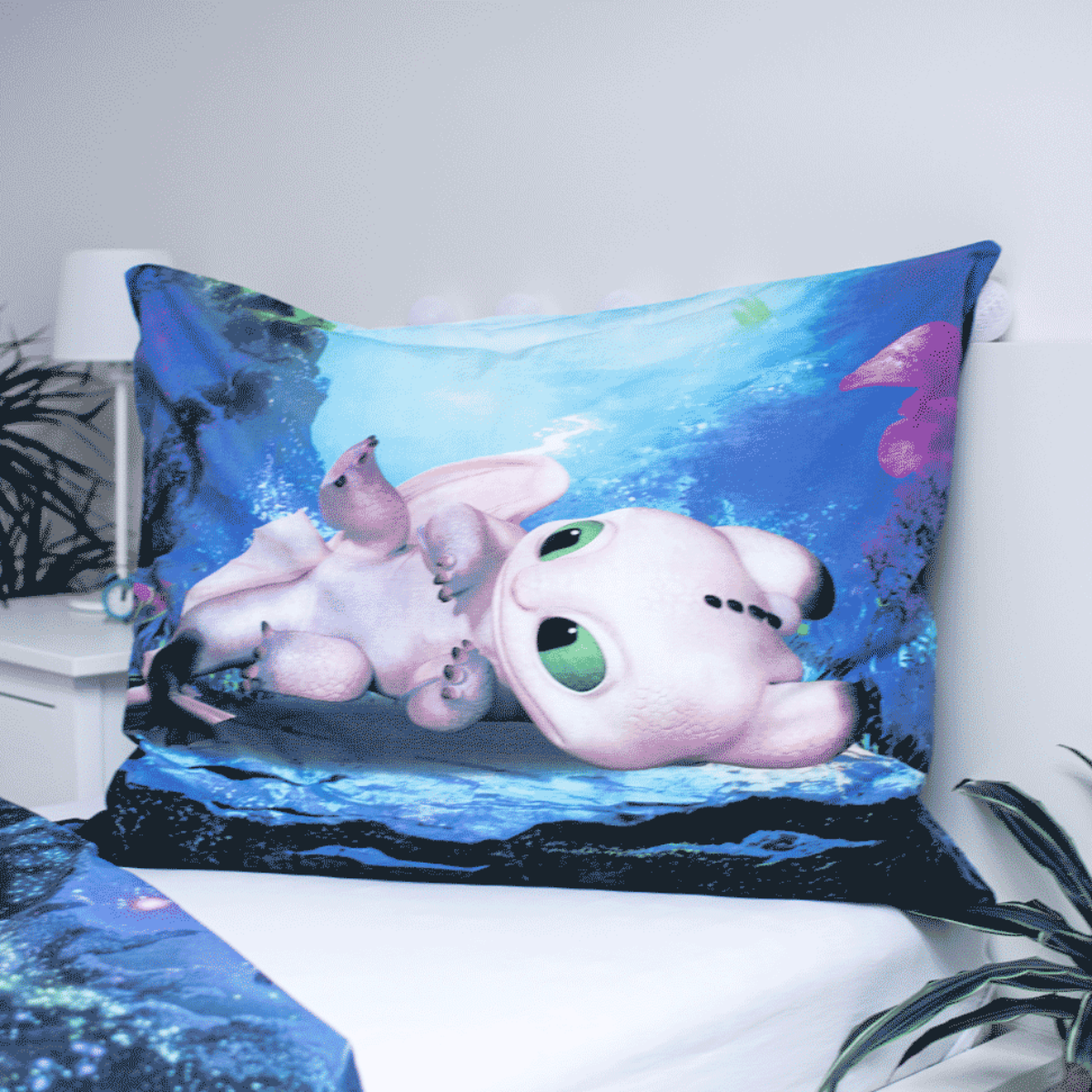 Ein Kissen mit einer Drachenillustration auf einem Bett. Der Drache ist weiß mit grünen Augen. Der Hintergrund ist blau mit Unterwassermotiven.