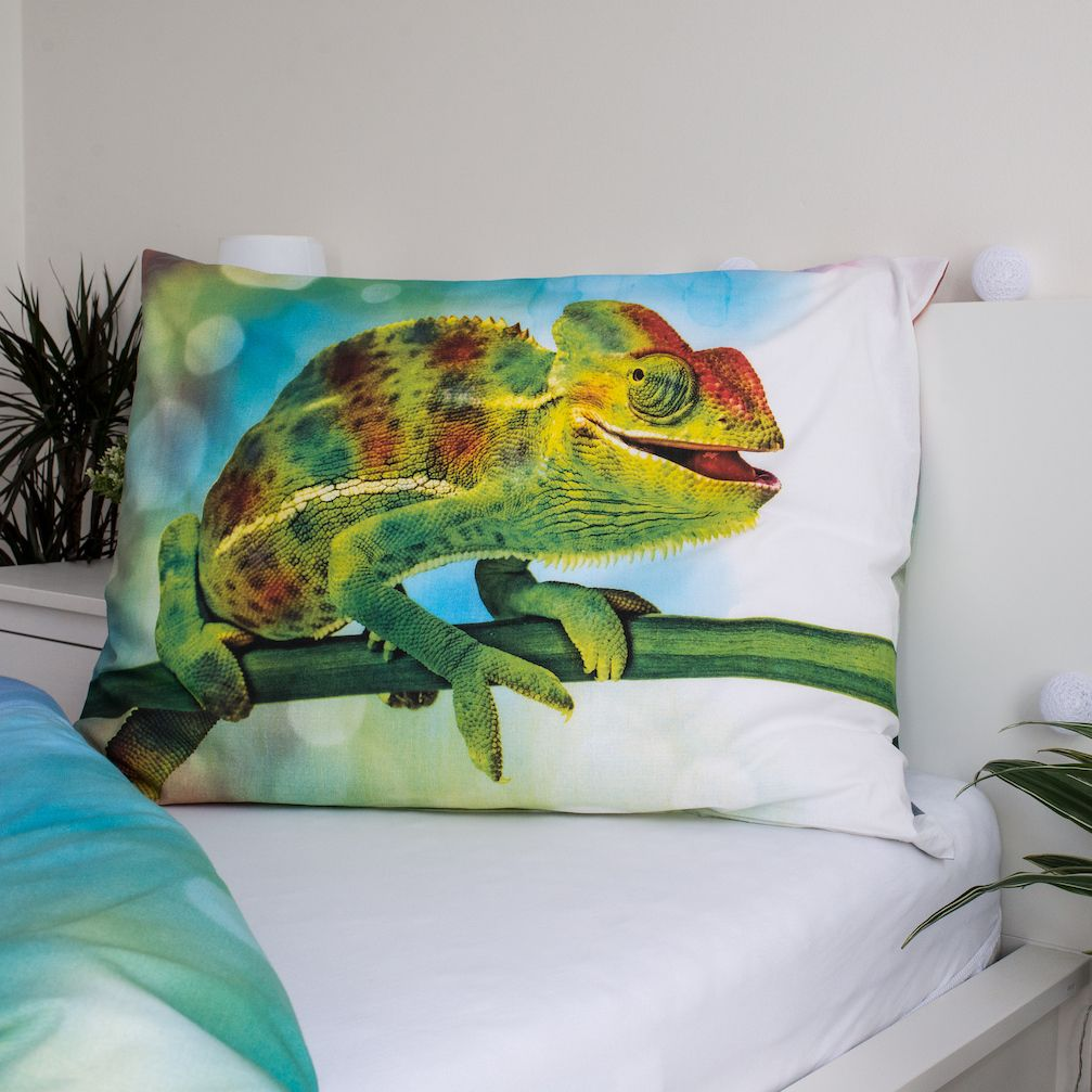 Kissen mit Chamäleon-Design. Das Chamäleon ist grün, gelb und rot und sitzt auf einem Ast. Das Kissen liegt auf einem weißen Bett.