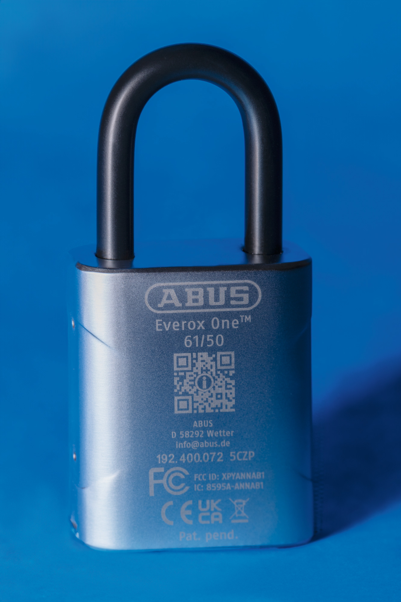 Ein silbernes ABUS Everox One Vorhängeschloss mit schwarzem Bügel, vor blauem Hintergrund. Details und QR-Codes sind sichtbar.