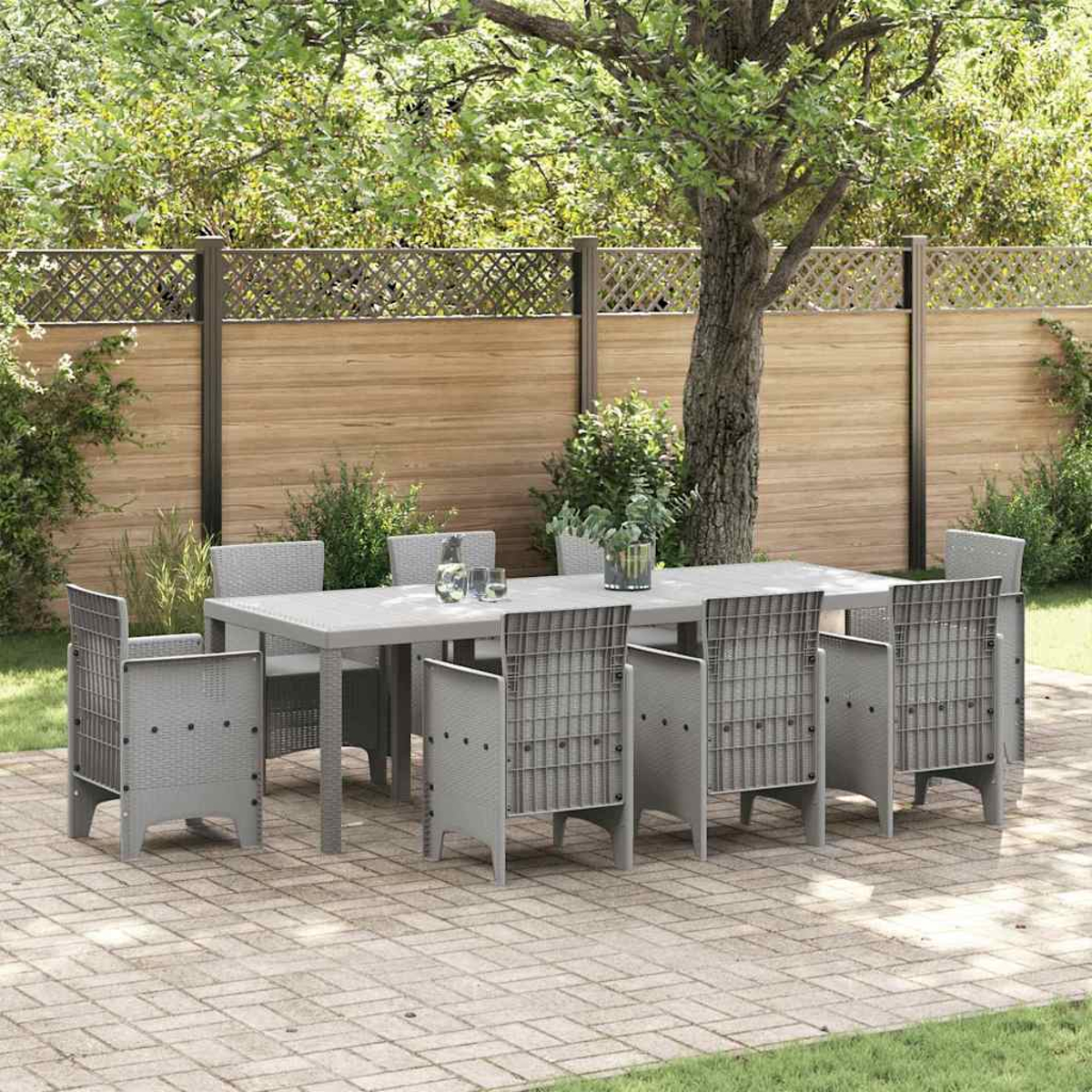 Essgruppe im Freien auf einer Terrasse. Grauer Tisch und Stühle. Holzzaun im Hintergrund. Grünes Gras und Baum sichtbar.