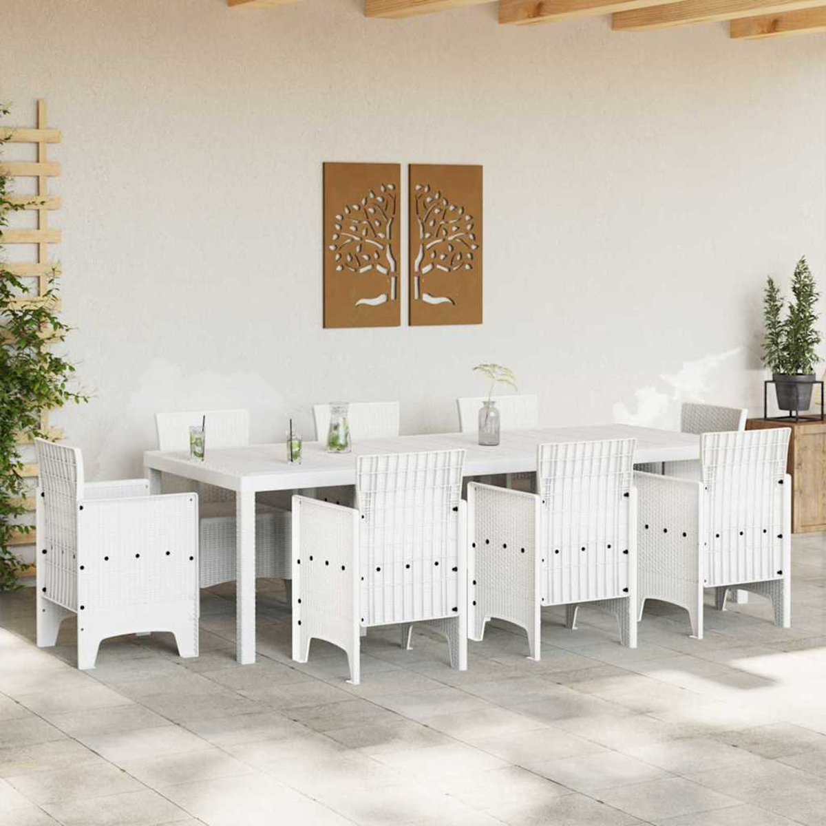 Essgruppe im Freien mit weißem Tisch und Stühlen. Braune Baumkunst an der Wand. Pflanzen und Getränke auf dem Tisch. Gepflasterte Terrasse.