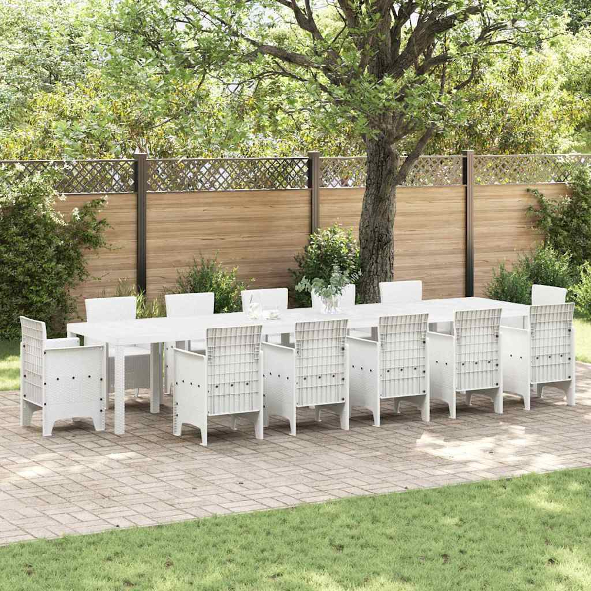 Ein weißes Ess-Set im Freien mit einem langen Tisch und Stühlen steht auf einer Ziegelterrasse, umgeben von Bäumen und einem Holzzaun.