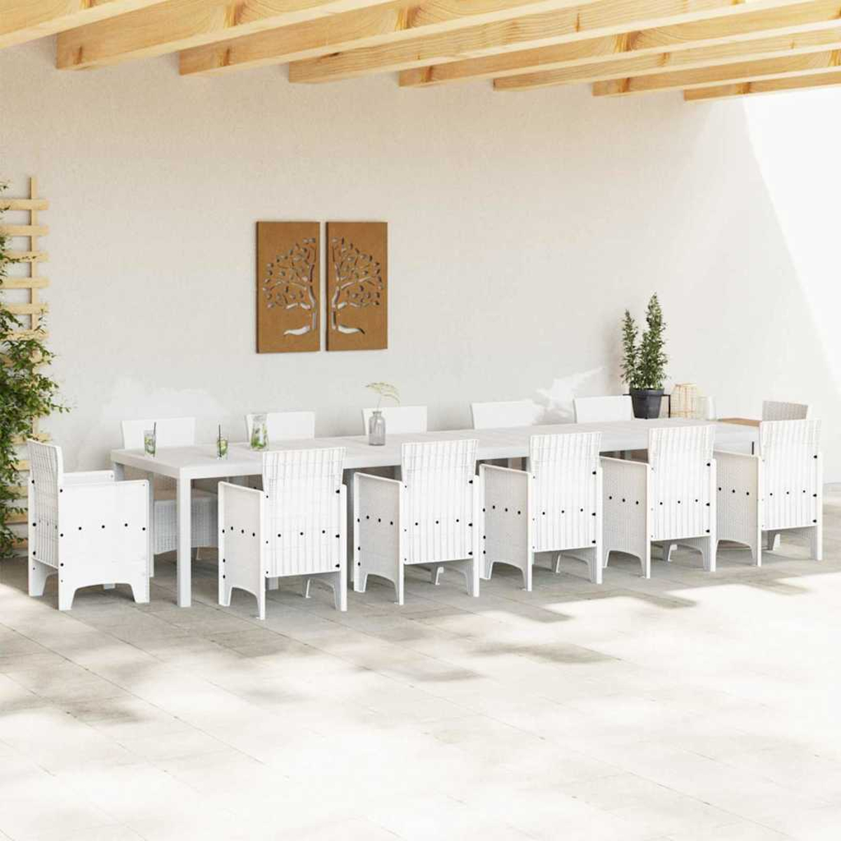 Essbereich im Freien. Weißer Tisch und Stühle unter einer Holzbalkenkonstruktion. Zwei Baumkunstwerke hängen an der weißen Wand.