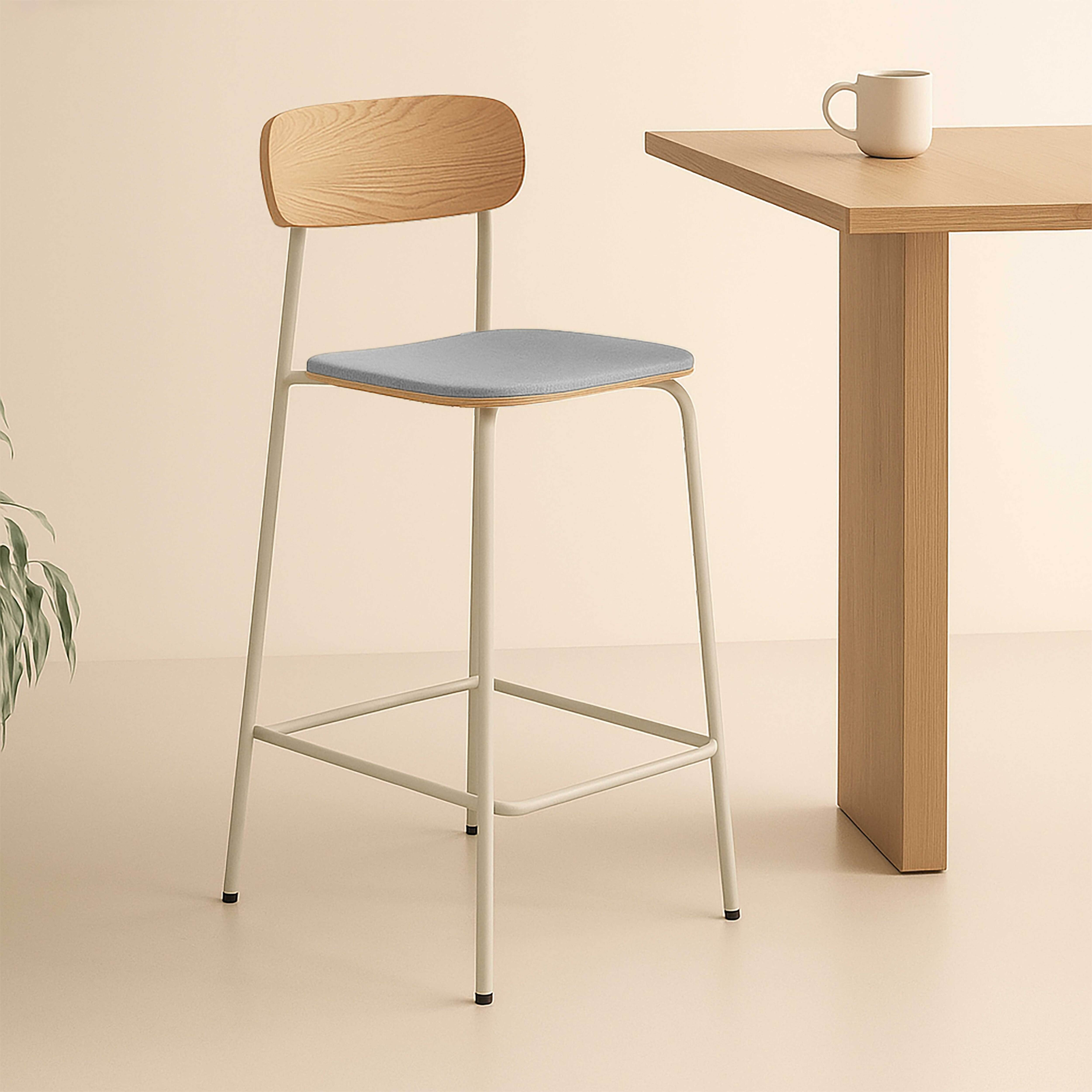 Ein moderner Barhocker mit grauem Sitz und hellem Holzrücken. Im Hintergrund ein Tisch mit einer Tasse.
