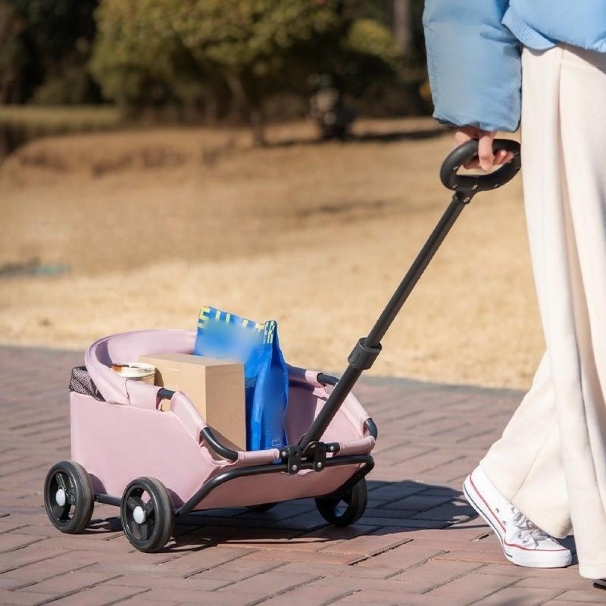 Eine Person zieht einen rosa Wagen mit schwarzen Rädern. Der Wagen trägt eine Kiste und Taschen. Die Person trägt weiße Hose und Schuhe.