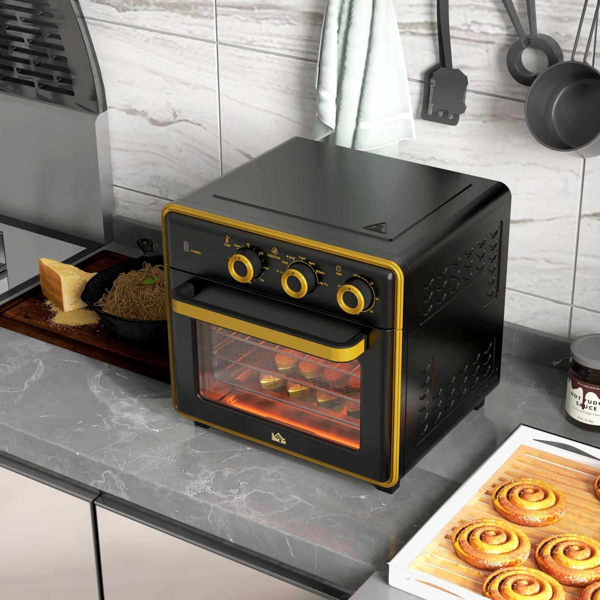 Ein schwarz-goldener Airfryer steht auf einer Arbeitsplatte, in der Nähe befinden sich Zimtschnecken und andere Kochutensilien.