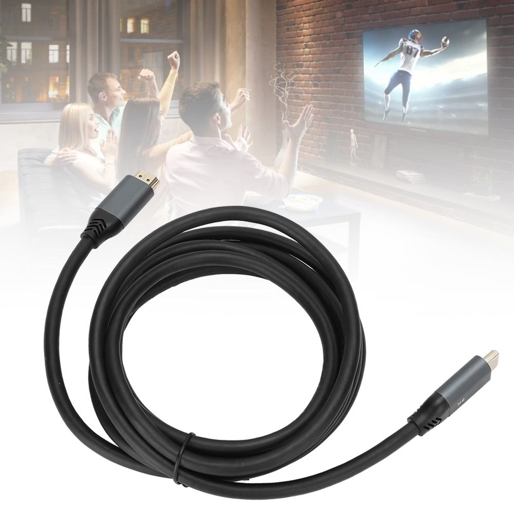 Ein schwarzes HDMI-Kabel ist im Vordergrund aufgerollt. Im Hintergrund schauen Leute ein Footballspiel im Fernsehen. Die Szene ist drinnen.