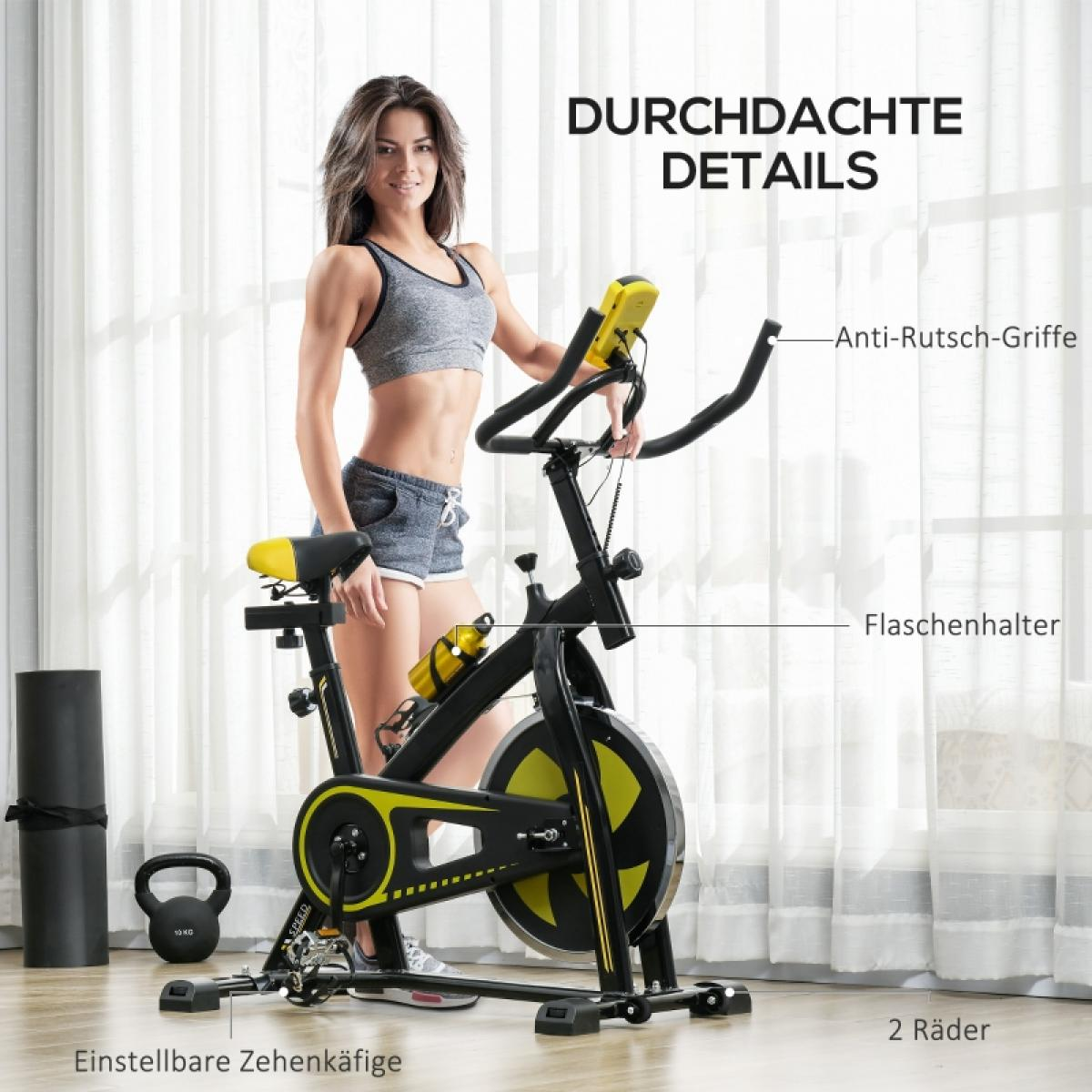 Eine Frau steht neben einem schwarz-gelben Trainingsrad. Eine Yogamatte und eine Kettlebell liegen auf dem Boden. Das Fahrrad hat eine Wasserflasche.