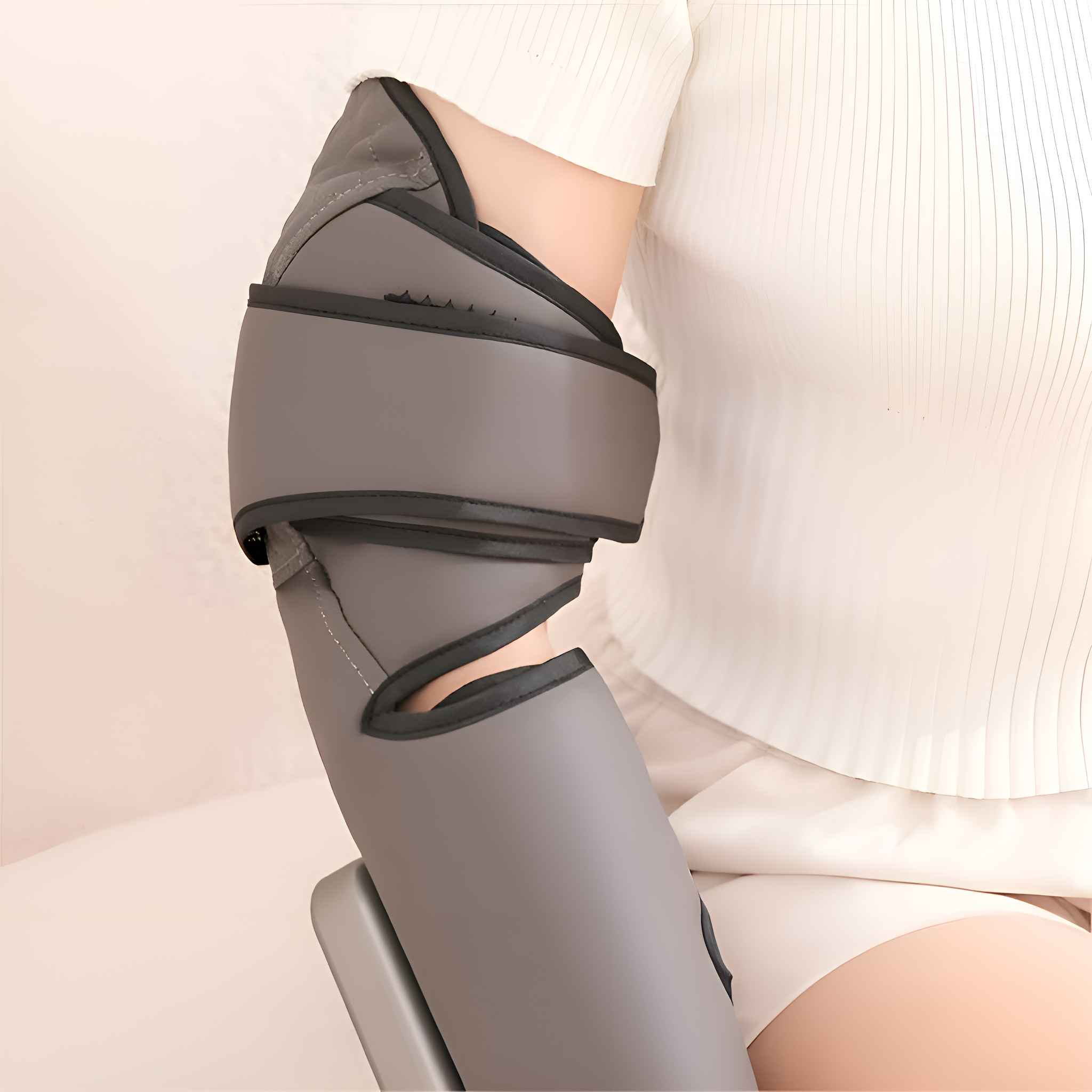 Ein graues Armmassagegerät ist um den Arm einer Person gewickelt. Die Person trägt ein weißes Hemd und Shorts. Der Hintergrund ist weiß.