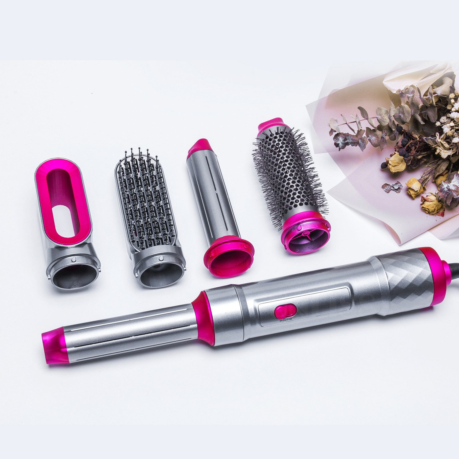Haarstyling-Set mit mehreren Aufsätzen, silber und rosa. Enthält eine Trocknerbasis und einen Strauß Trockenblumen auf weißer Oberfläche.
