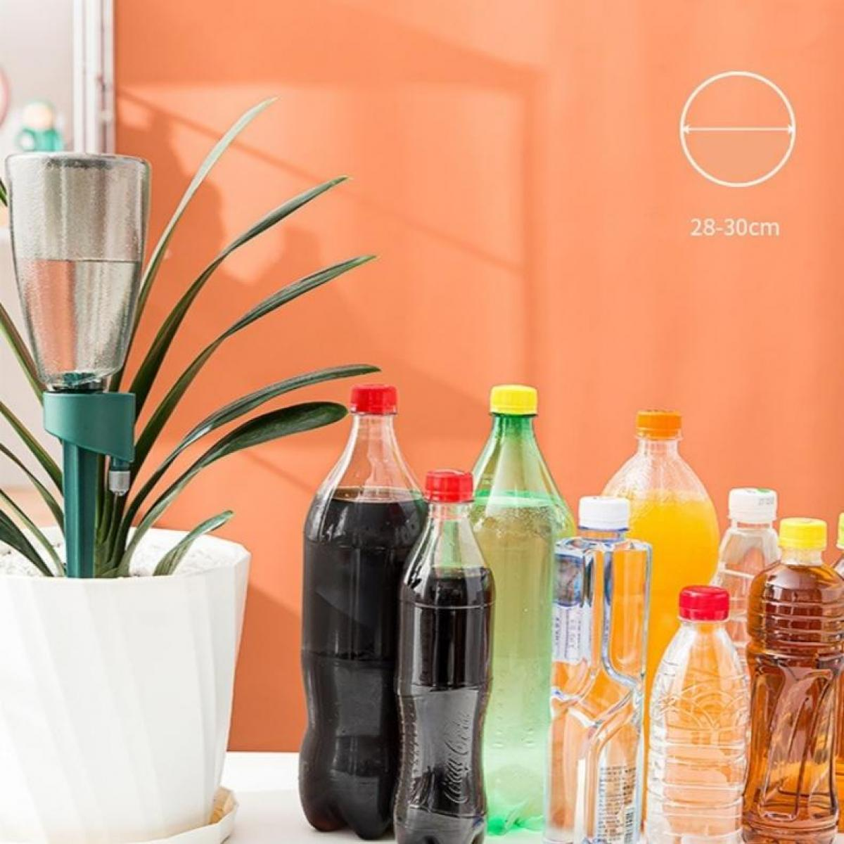 Pflanze mit Bewässerungsgerät. Verschiedene Flaschen Soda und Saft sind im Hintergrund. Orange Wand. Weißer Tisch.