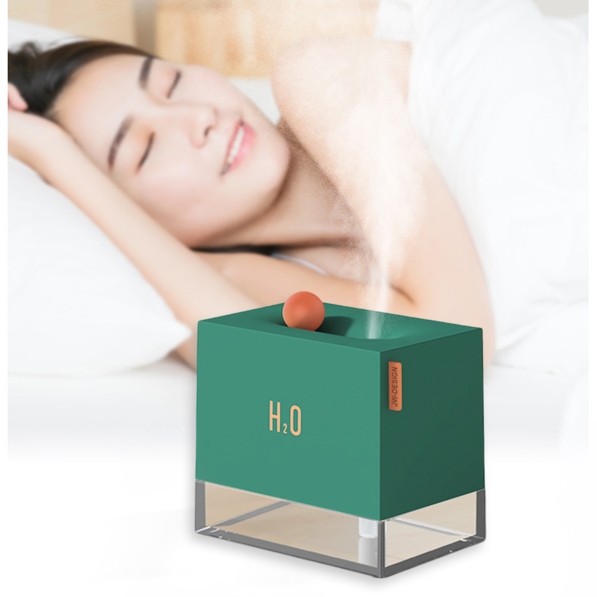 Eine Frau schläft im Bett. Ein grüner Luftbefeuchter mit einer orangefarbenen Kugel befindet sich im Vordergrund. H2O ist auf dem Luftbefeuchter aufgedruckt.