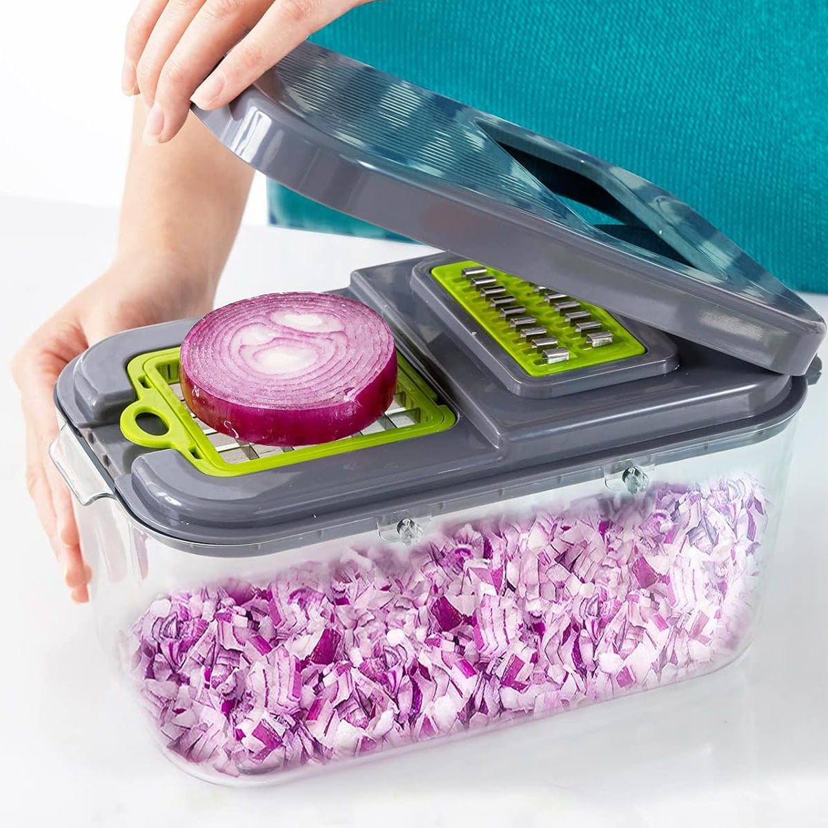 Eine Person benutzt einen grauen und transparenten Gemüseschneider mit einer roten Zwiebelscheibe obenauf. Gehackte Zwiebelstücke füllen den Behälter.