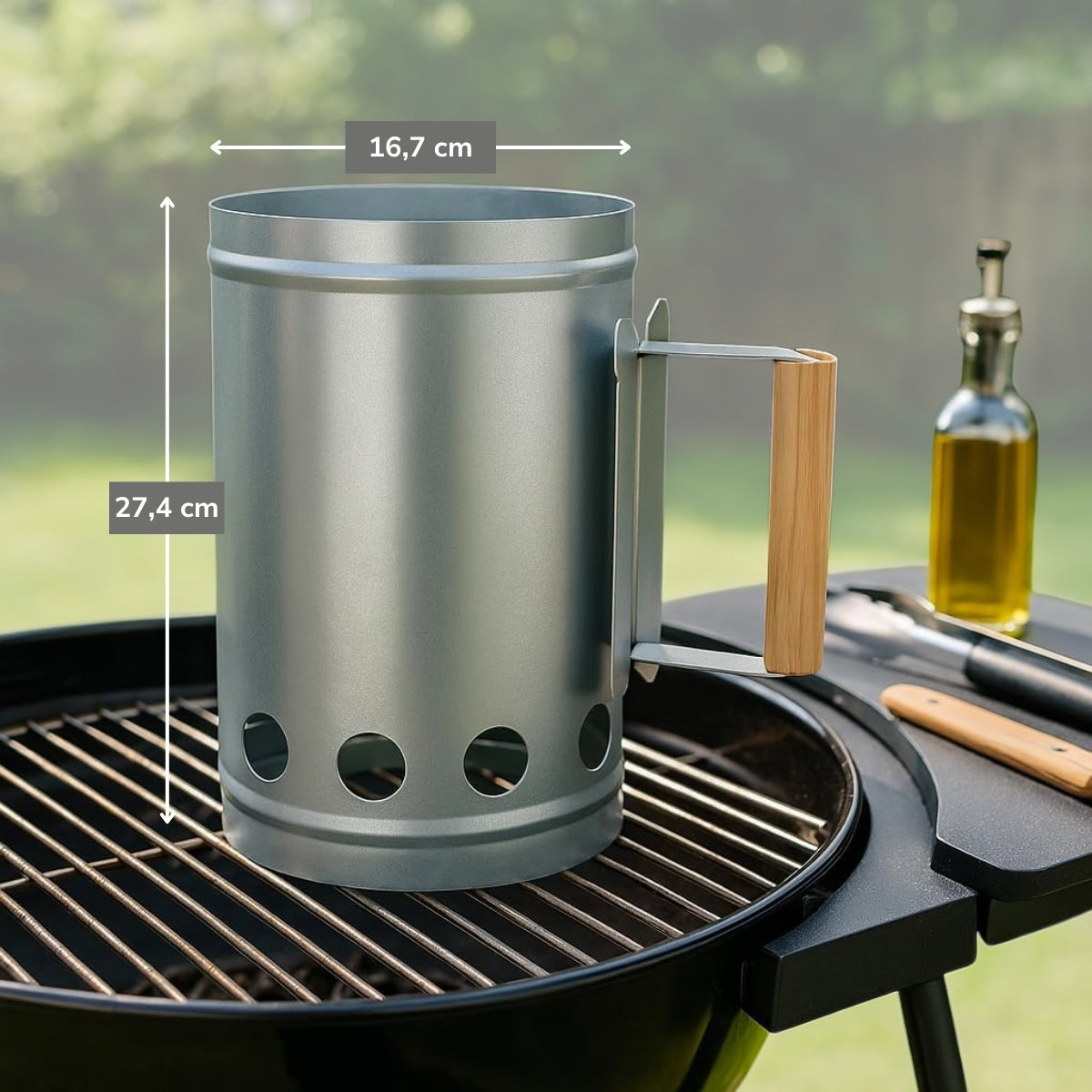 A silver charcoal chimney with a wooden handle sits on a grill. An oil bottle and tongs are nearby.